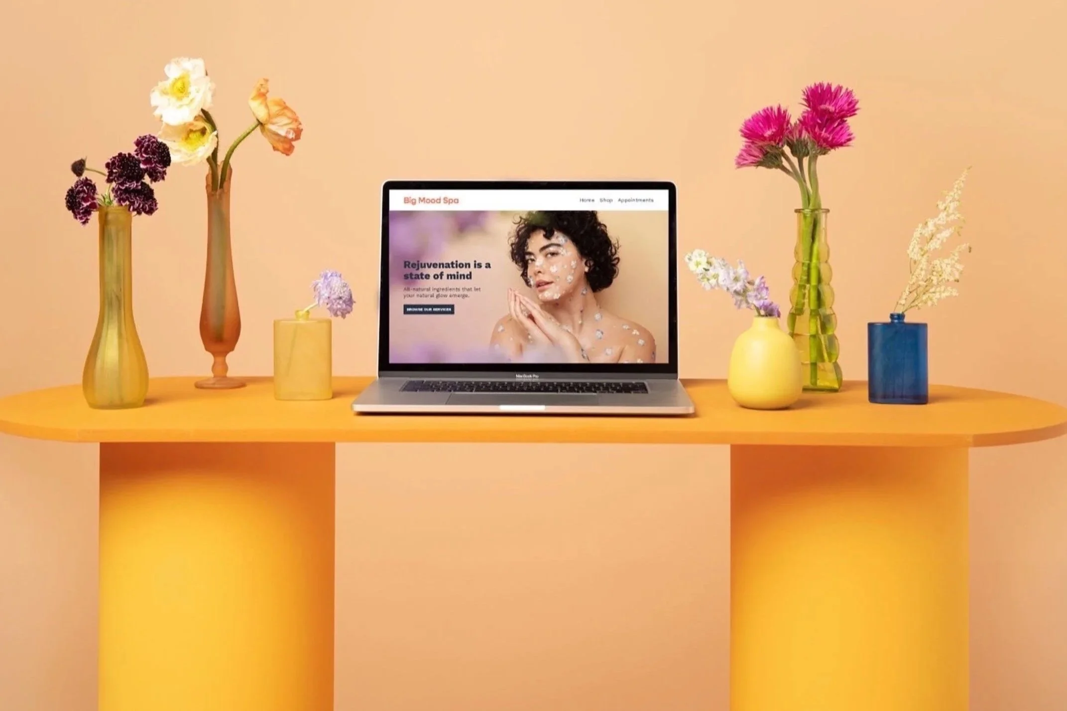 Laptop with spa website shown sitting on a table surrounded by vases of flowers. 