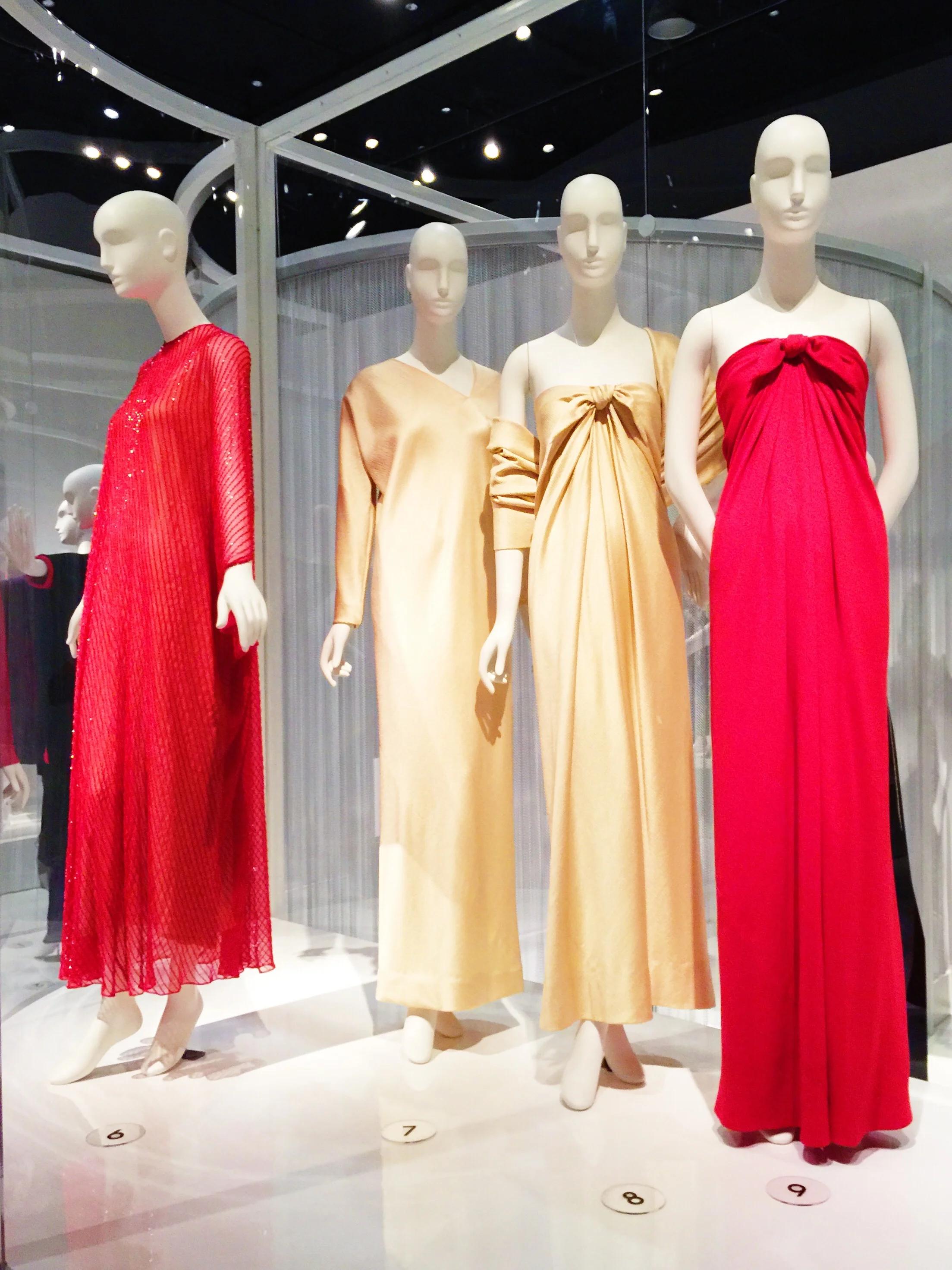 Left to Right Halston Red evening caftan, beaded nylon, circa 1977, New York Gold evening dress, hammered silk satin, circa 1977, New York Gold "sarong" dress and stole, hammered silk satin, 1976, New York Red "sarong" dress, silk crepe, circa 1976, New York
