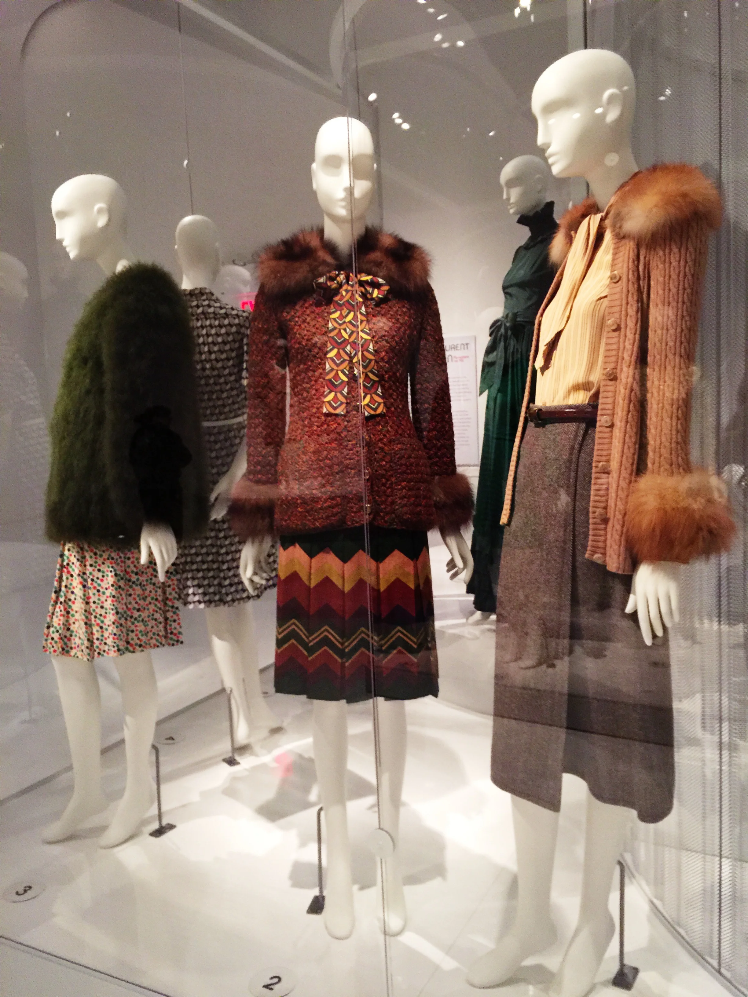 Left to Right Saint Laurent Rive Gauche Green "chubby" style coat, marabou feathers, 1971, France Polka-dot shirt dress, printed rayon crepe, circa 1971, France Multi-color ensemble, wool, silk, and fur, 1972, Paris Saint Laurent Rive Gauche Camel sweater, wool and fur, 1973, France Herringbone skirt, wool, 1969, France