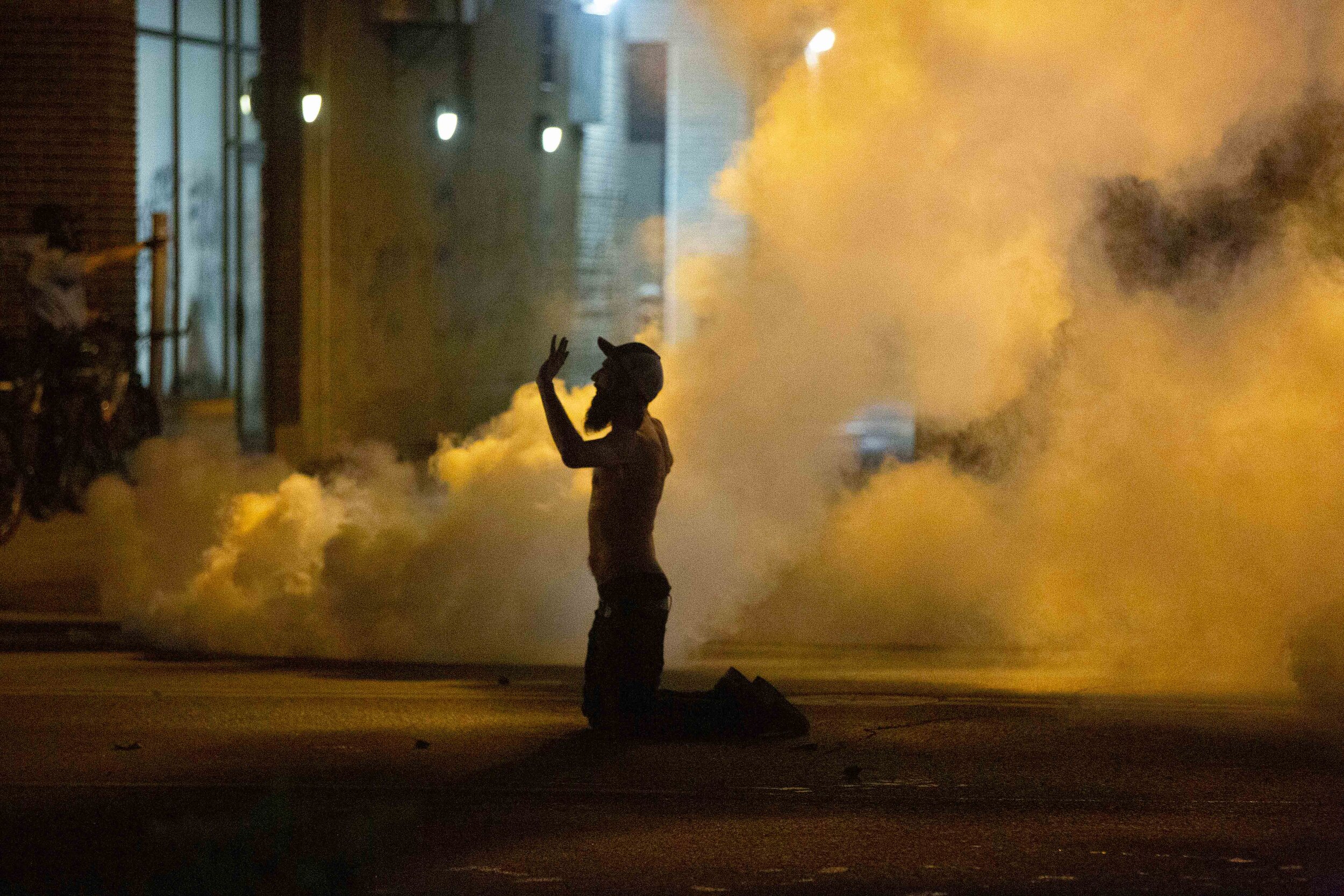  A protester holds his hands up in front of a police line as tear gas goes off around him during the second night of protest over the police killing of George Floyd in Minneapolis, Minnesota on May 27, 2020. 