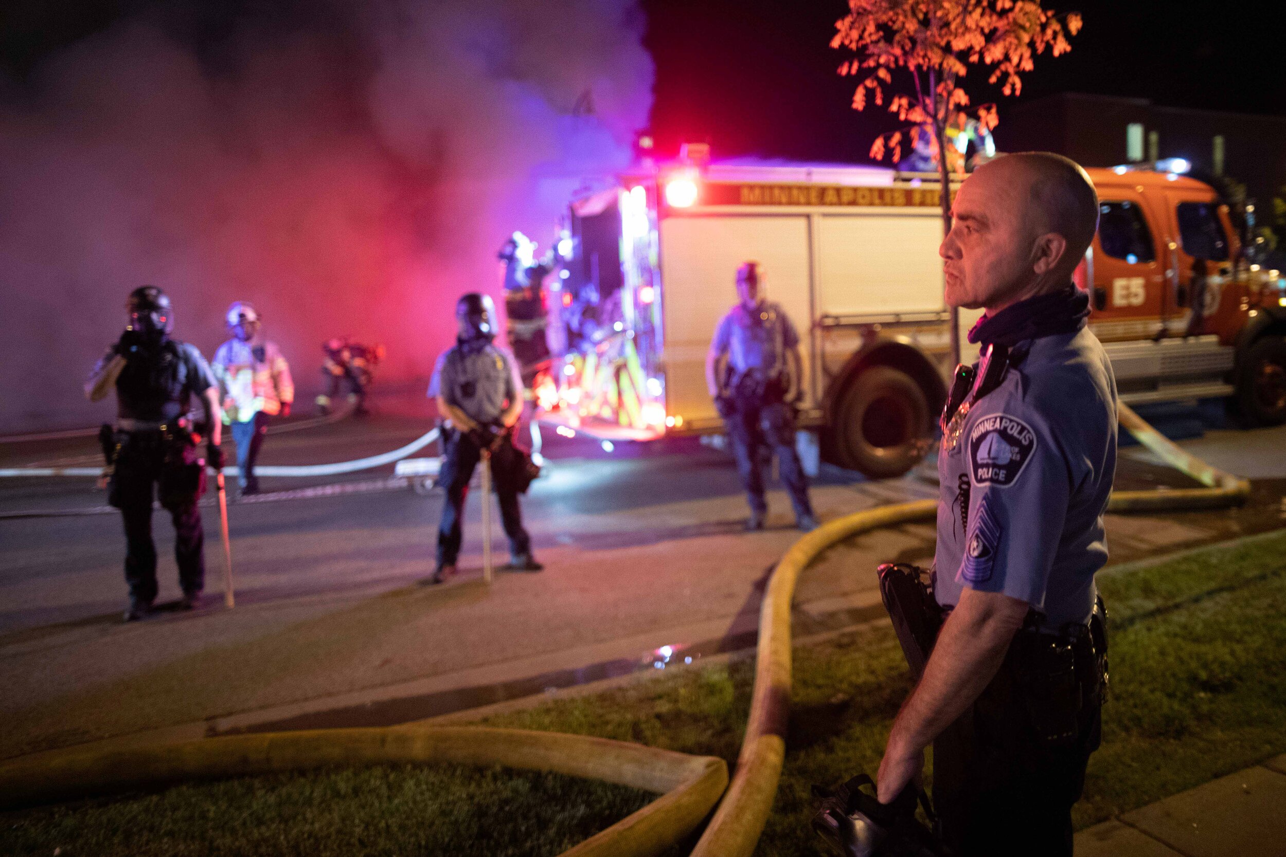  An officer with the Minneapolis Police Department stands in front of other officers as they create a police line to protect the fire department as they extinguish a fire set during a riot over the police killing of George Floyd in Minneapolis, Minne