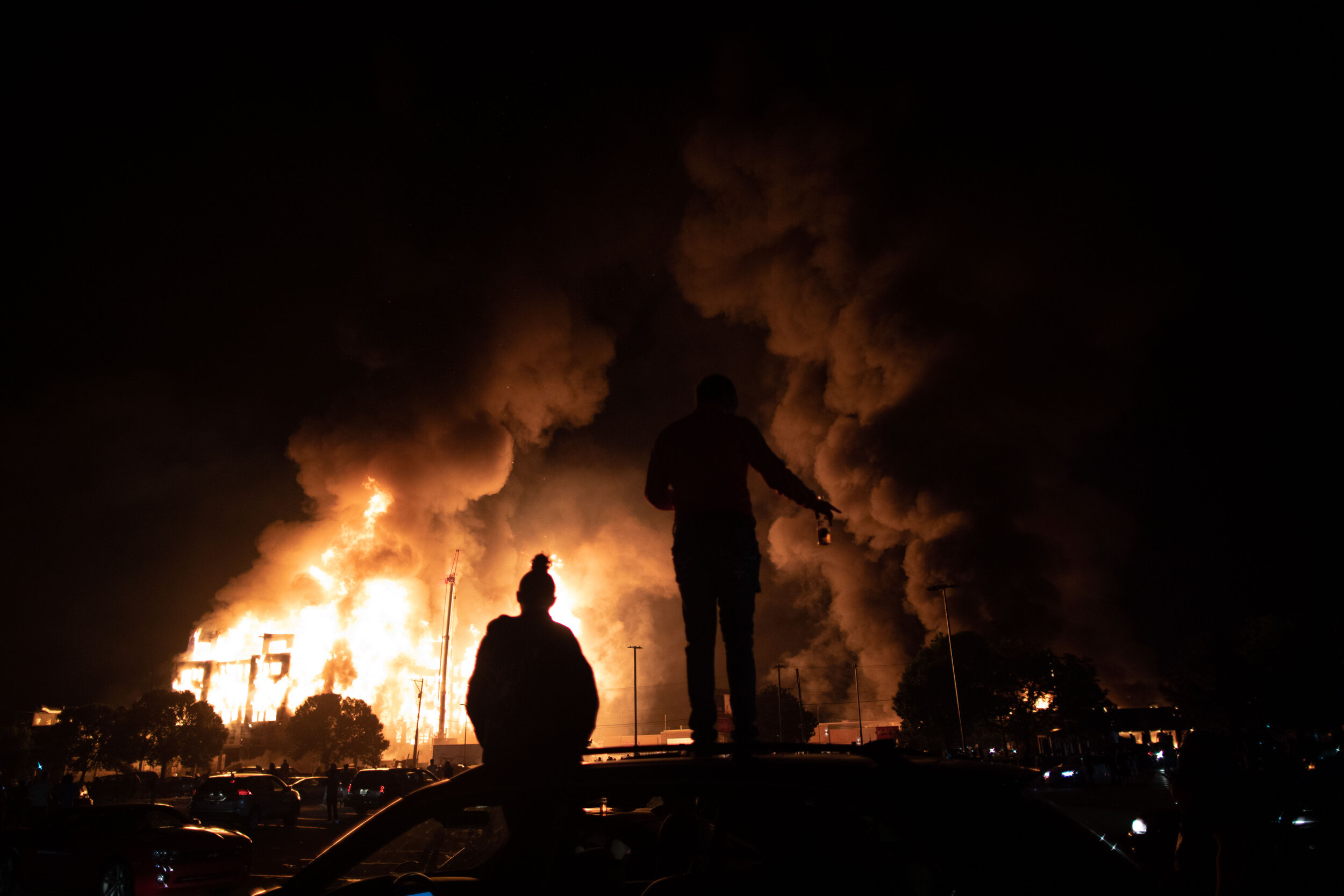  Standing and sitting on top of a car, 2 people watch a190 unit affordable housing complex that was under construction burns after it was set on fire during a riot over the police killing of George Floyd in Minneapolis, Minnesota on May 28. 