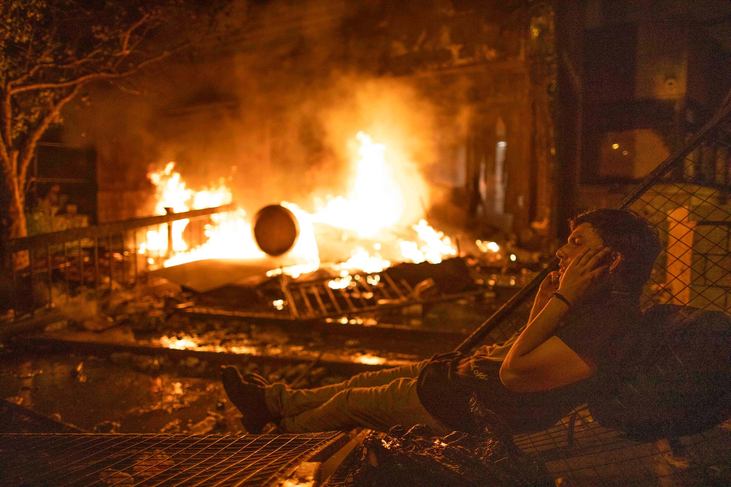  A protester sits on a fence in front of a fire started at the Minneapolis 3rd police precinct during a riot over the killing of George Floyd on May 28, 2020. 