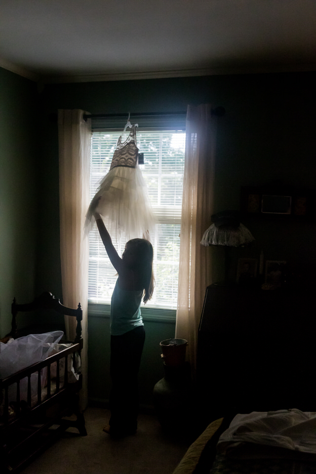  A flower girl reaches for her dress while its hanging in a window 