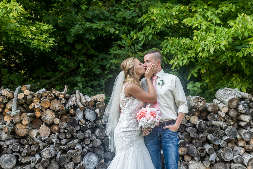  The bride and groom pose for a photo in front of a wood pile at Bridgeton Barn 