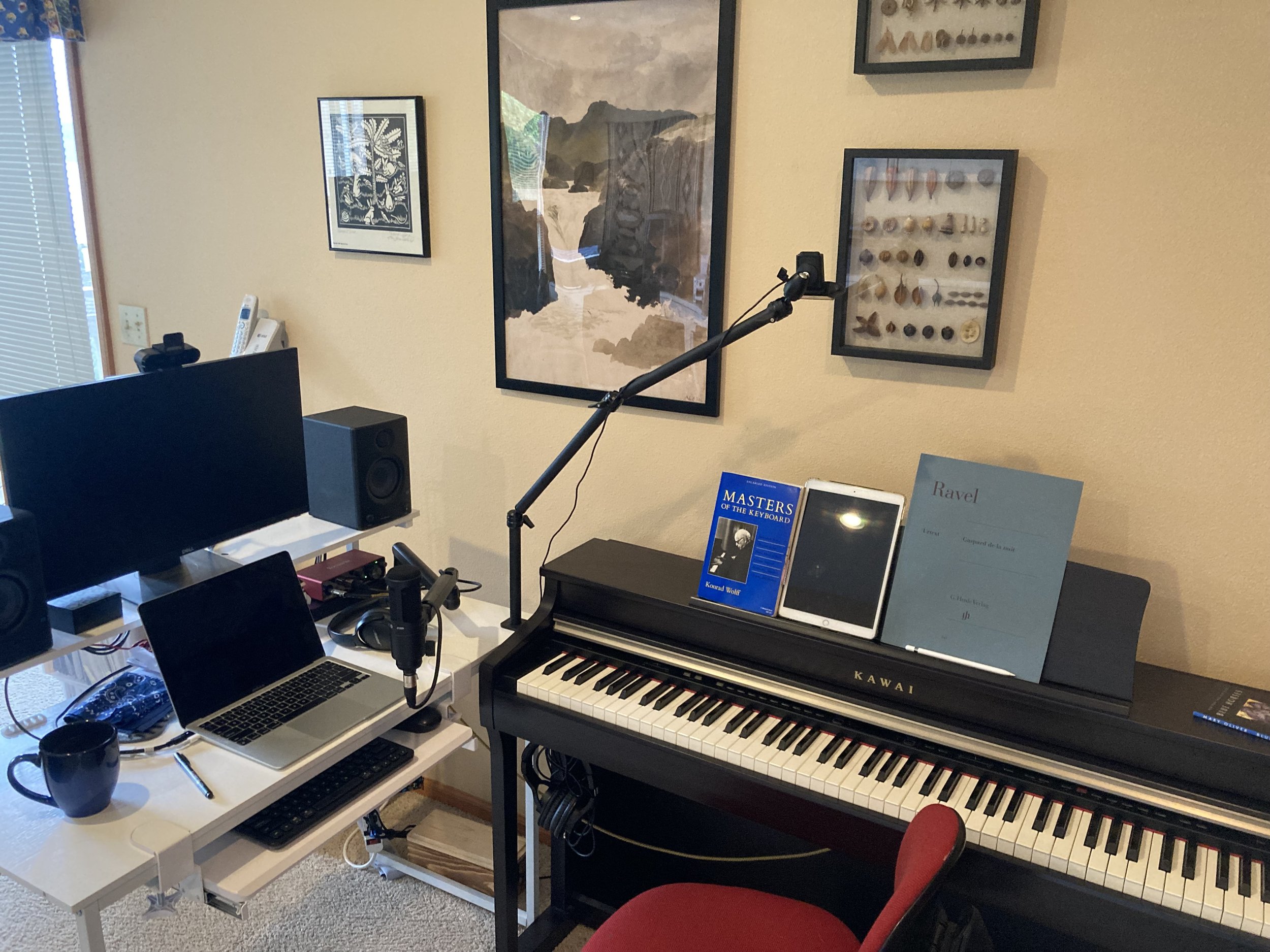 Office space with a digital piano, a tablet, and music scores next to a desk with a laptop and microphone