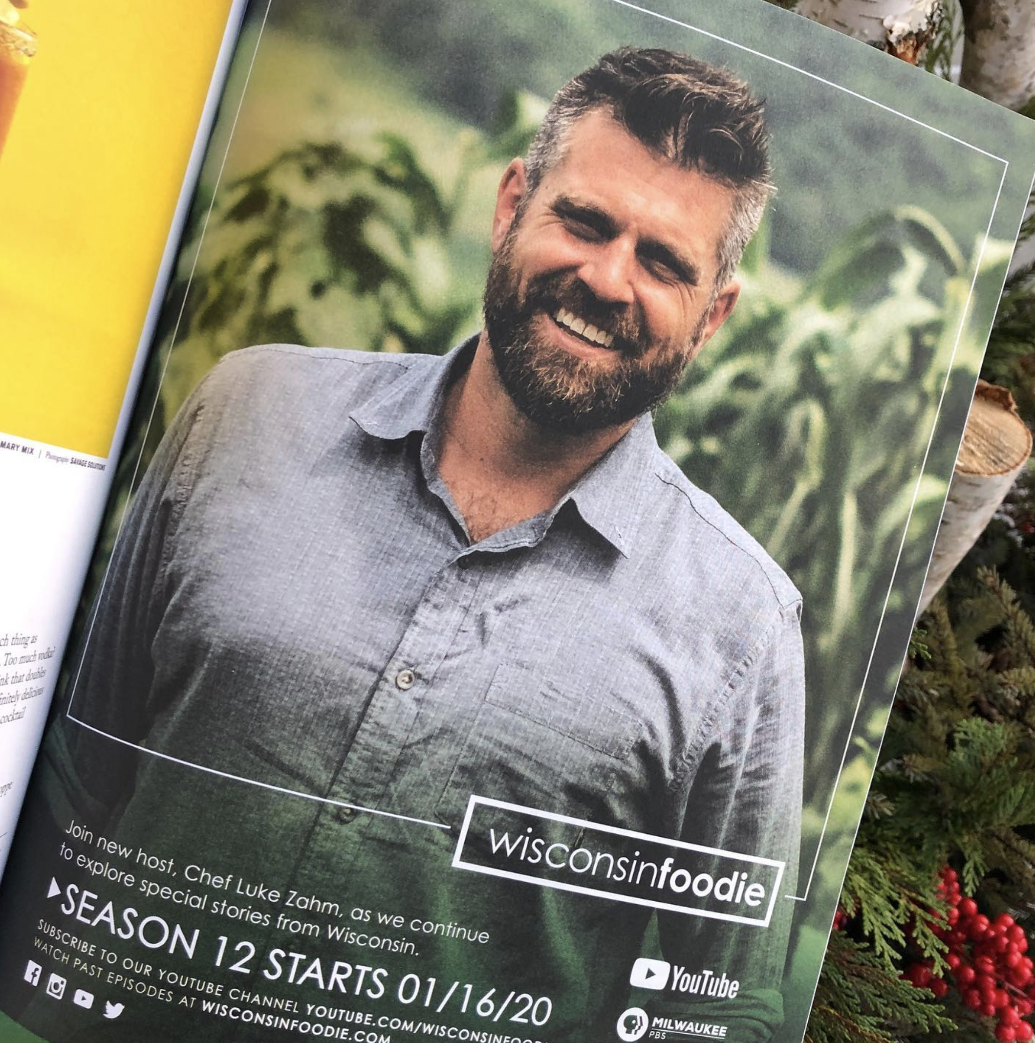 Man smiling on a magazine page promoting "Wisconsin Foodie" with text about a new host and the start of Season 12 on January 16, 2020. The background shows greenery.