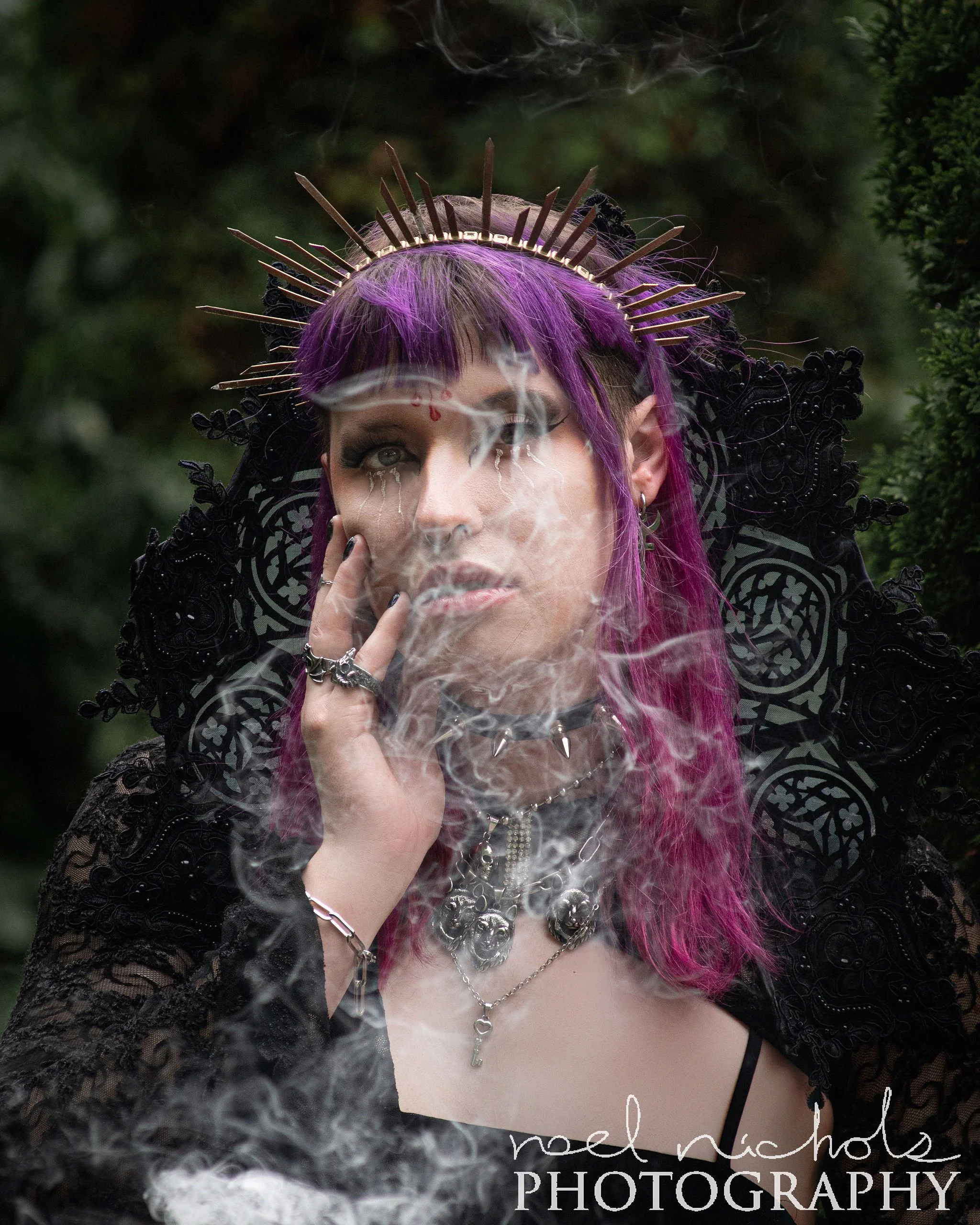 A dark and elegant portrait of a woman with purple hair and a halo crown. She wears all black and a lace collar with stainless steel jewelry. There is a mysterious fog that obscures part of the image. 