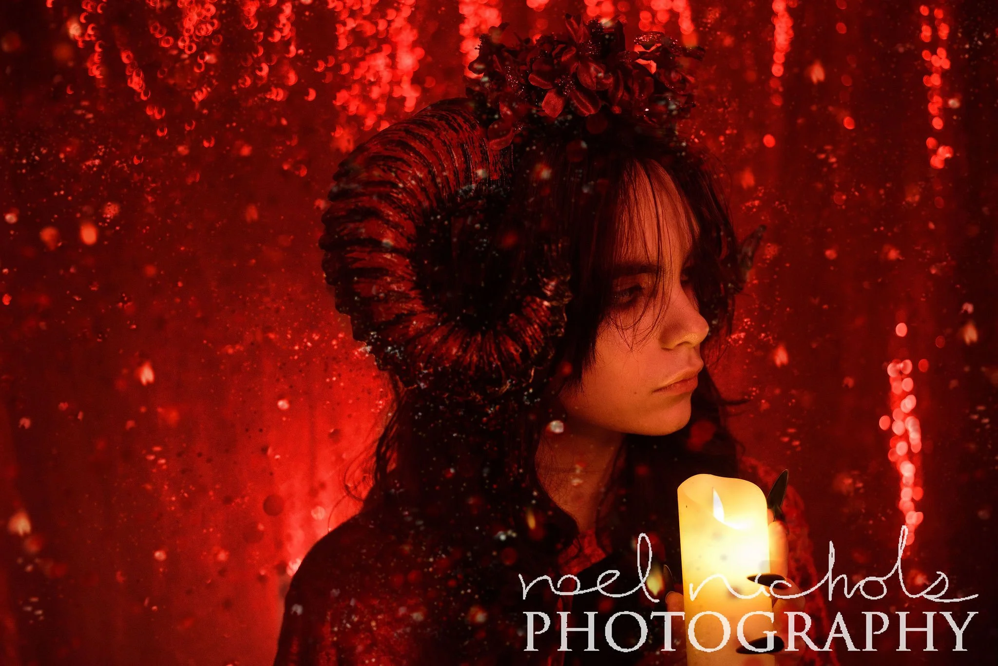 young woman with ram horns holding a candle in front of a red sequin background