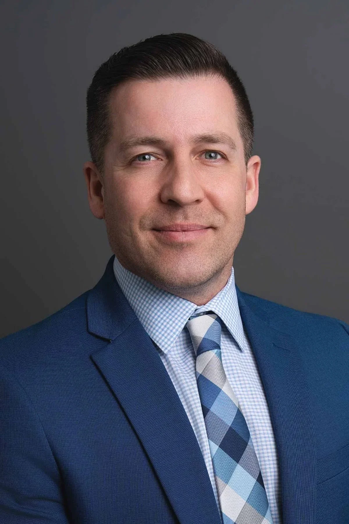 Professional corporate business headshot of a Winnipeg professional photographed in a studio on a charcoal grey backdrop.
