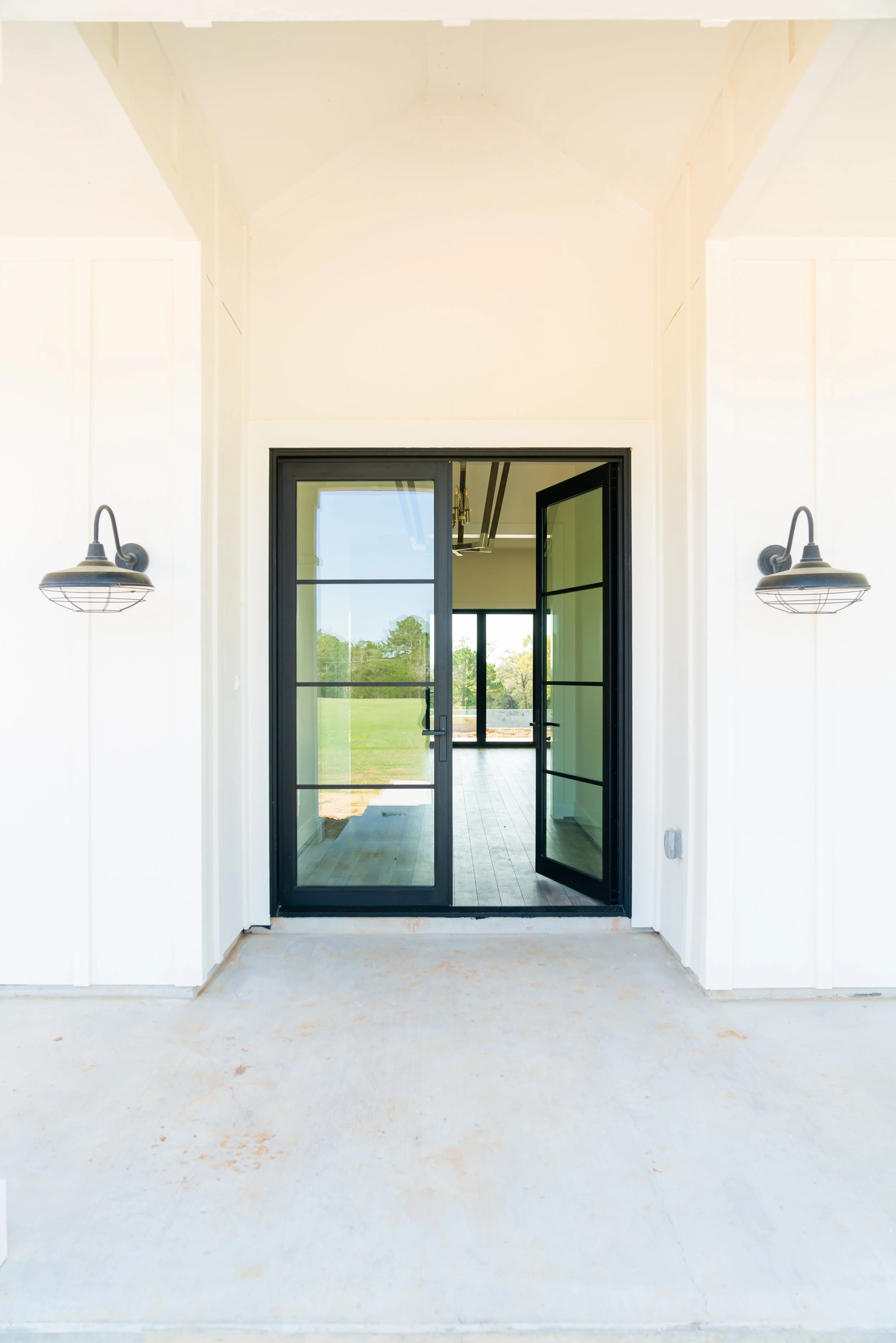 Open black-framed glass sliding doors leading to a bright room with large windows showing a green outdoor landscape.