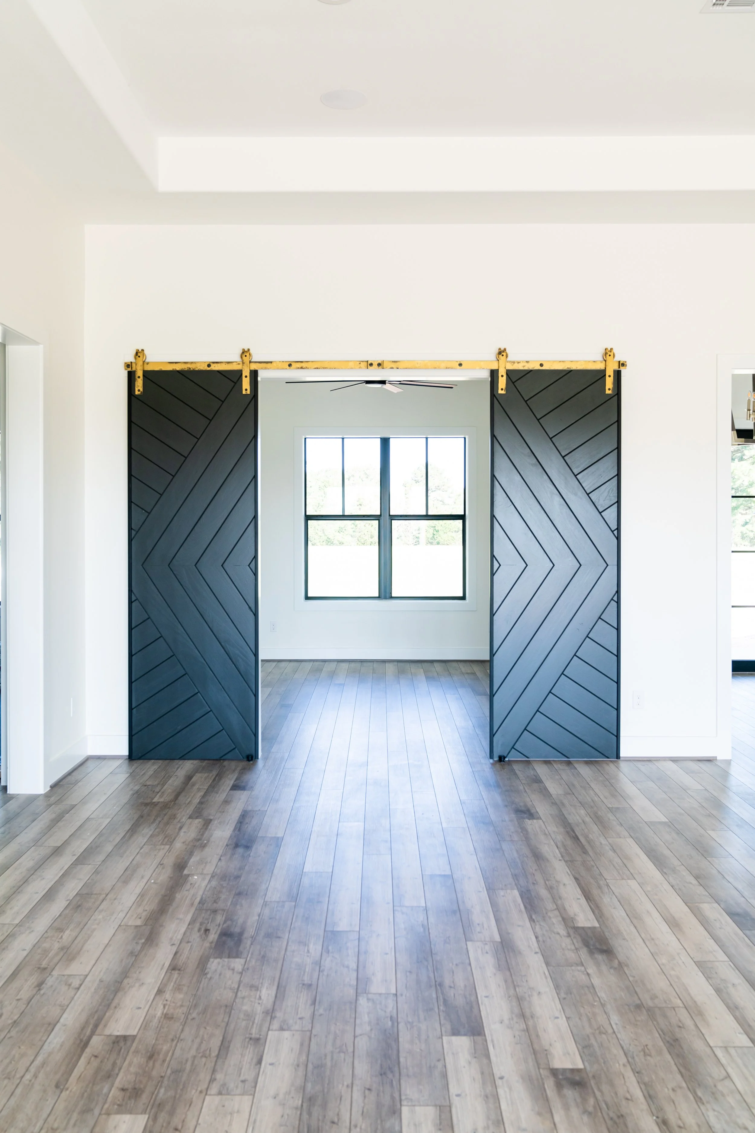Modern living room with black sliding barn doors, white walls, large window, and wood flooring.