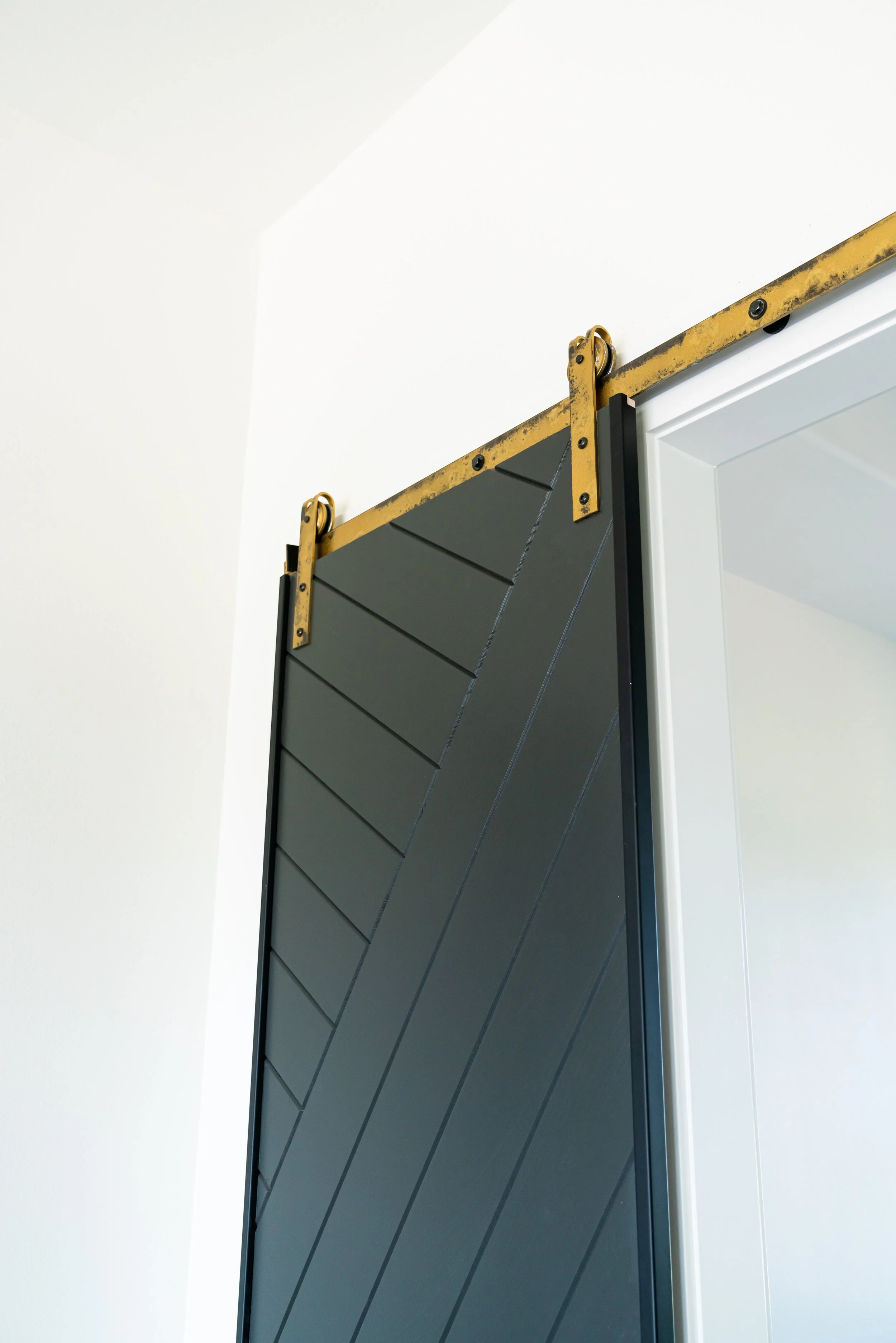 Close-up of a sliding barn door with black panels and gold hardware on a white wall.