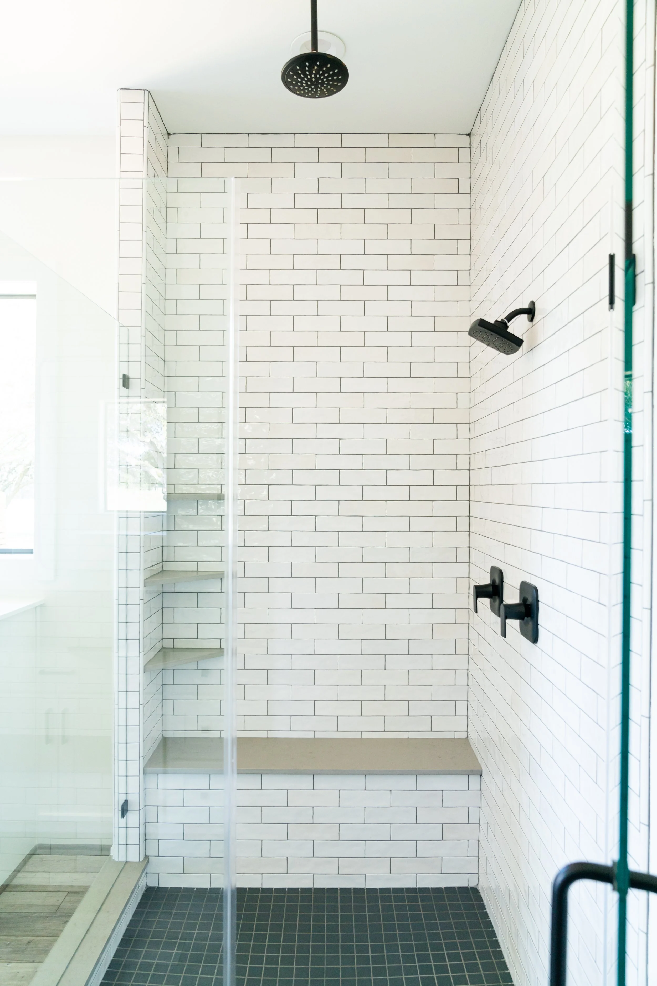 Modern walk-in shower with white subway tile walls, black fixtures, and a built-in bench.