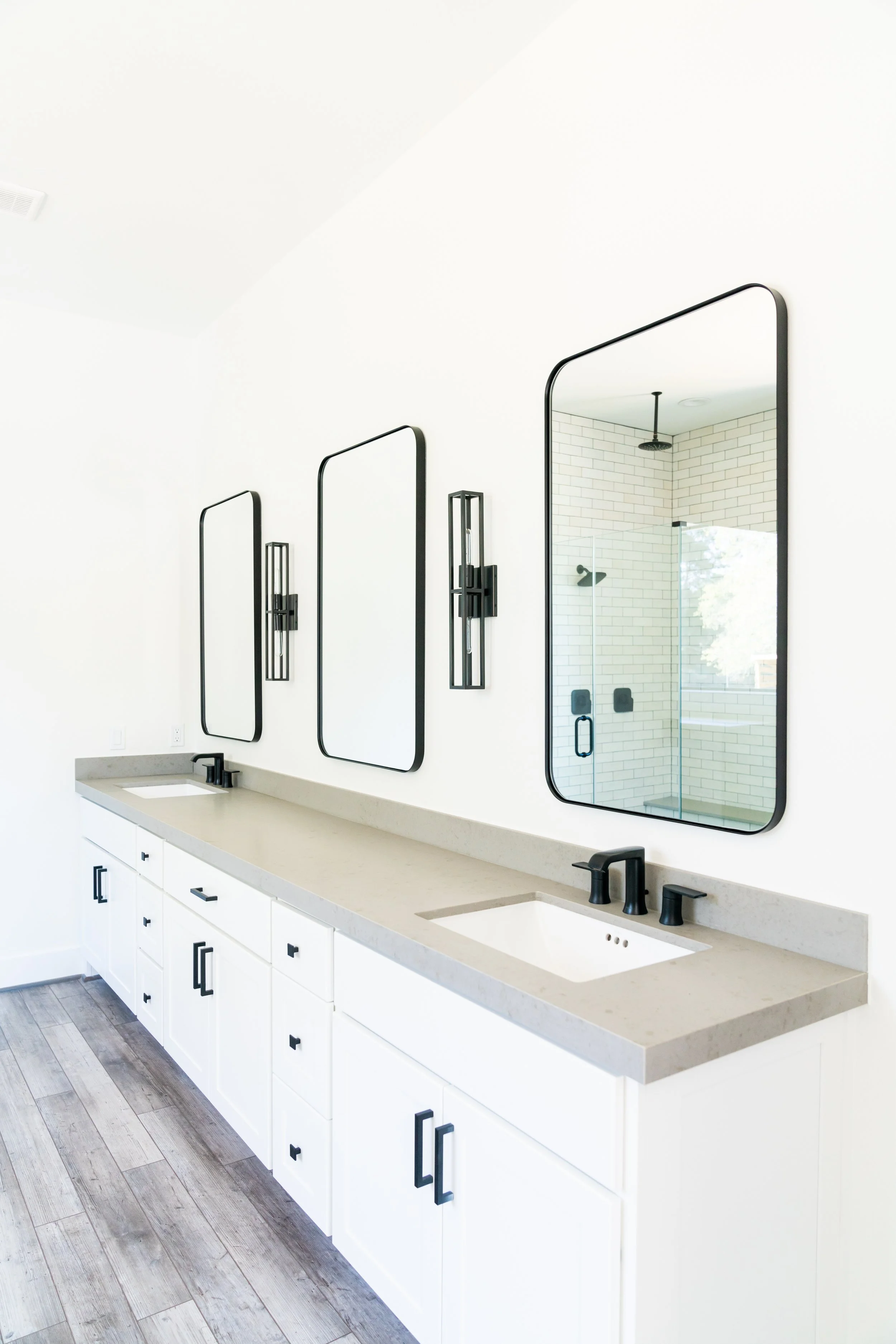 Modern bathroom with white vanity, three mirrors, black fixtures, and a glass shower with white subway tile.
