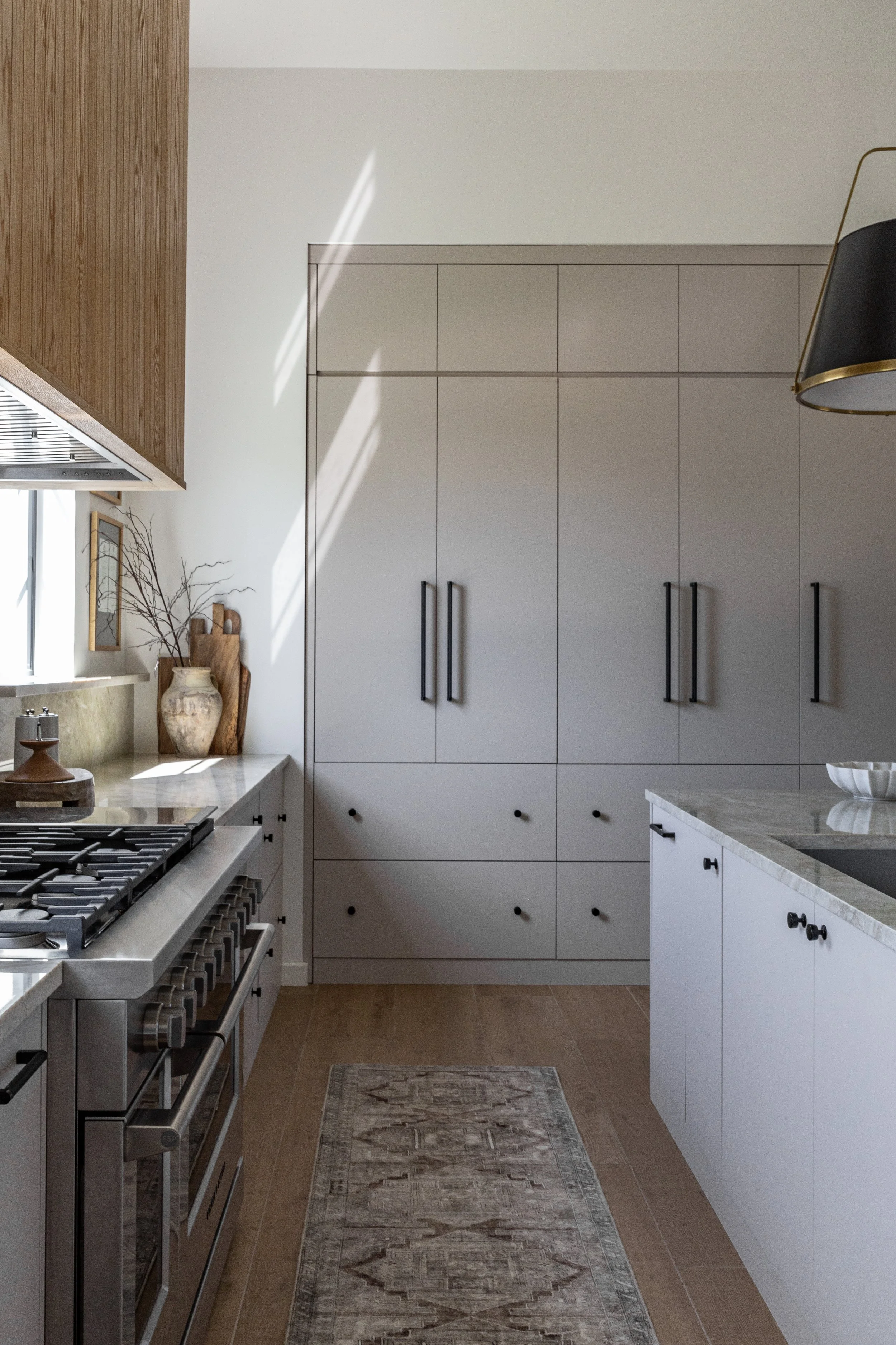 Modern kitchen with white cabinetry, stainless steel stove, marble countertops, and decorative vases with branches on the window sill.