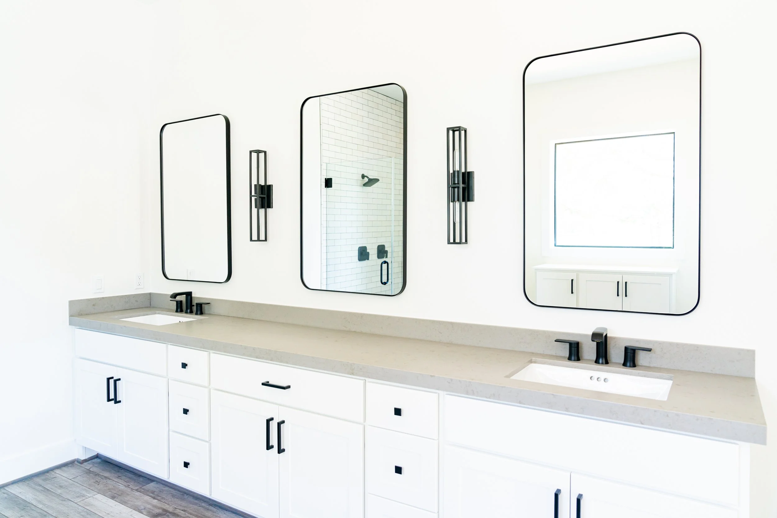 Modern bathroom with white vanity, black fixtures, three large mirrors, and a shower with white subway tiles.