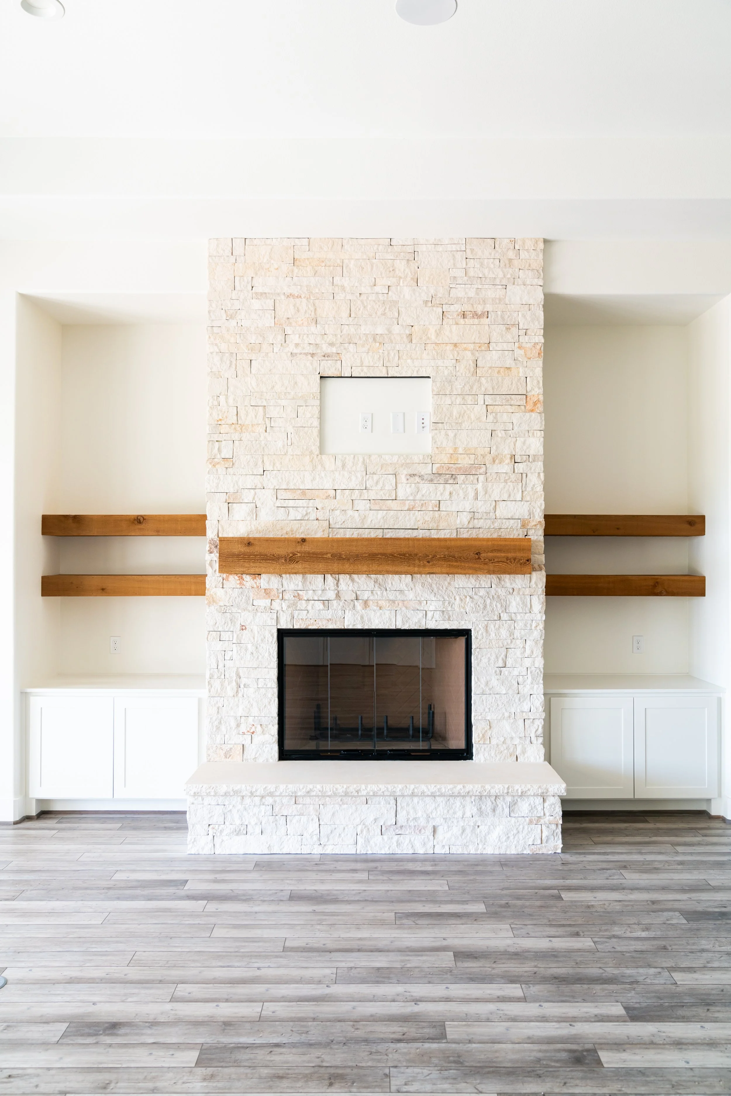Living room with a white stone fireplace flanked by two built-in cabinets, dark wood floors, and floating wooden shelves.