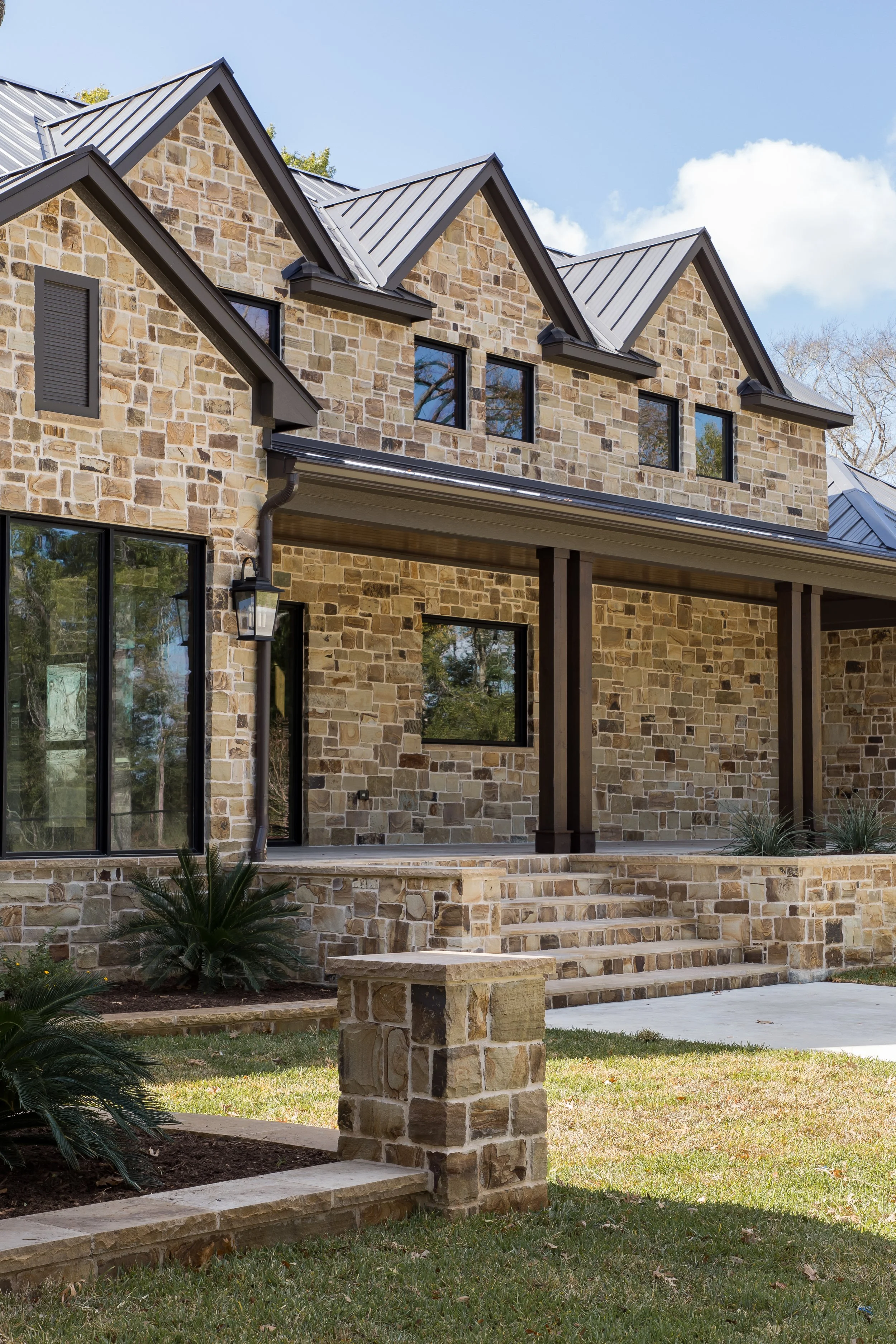Modern black house with metal roof, front porch, and landscaped garden, under a blue sky.