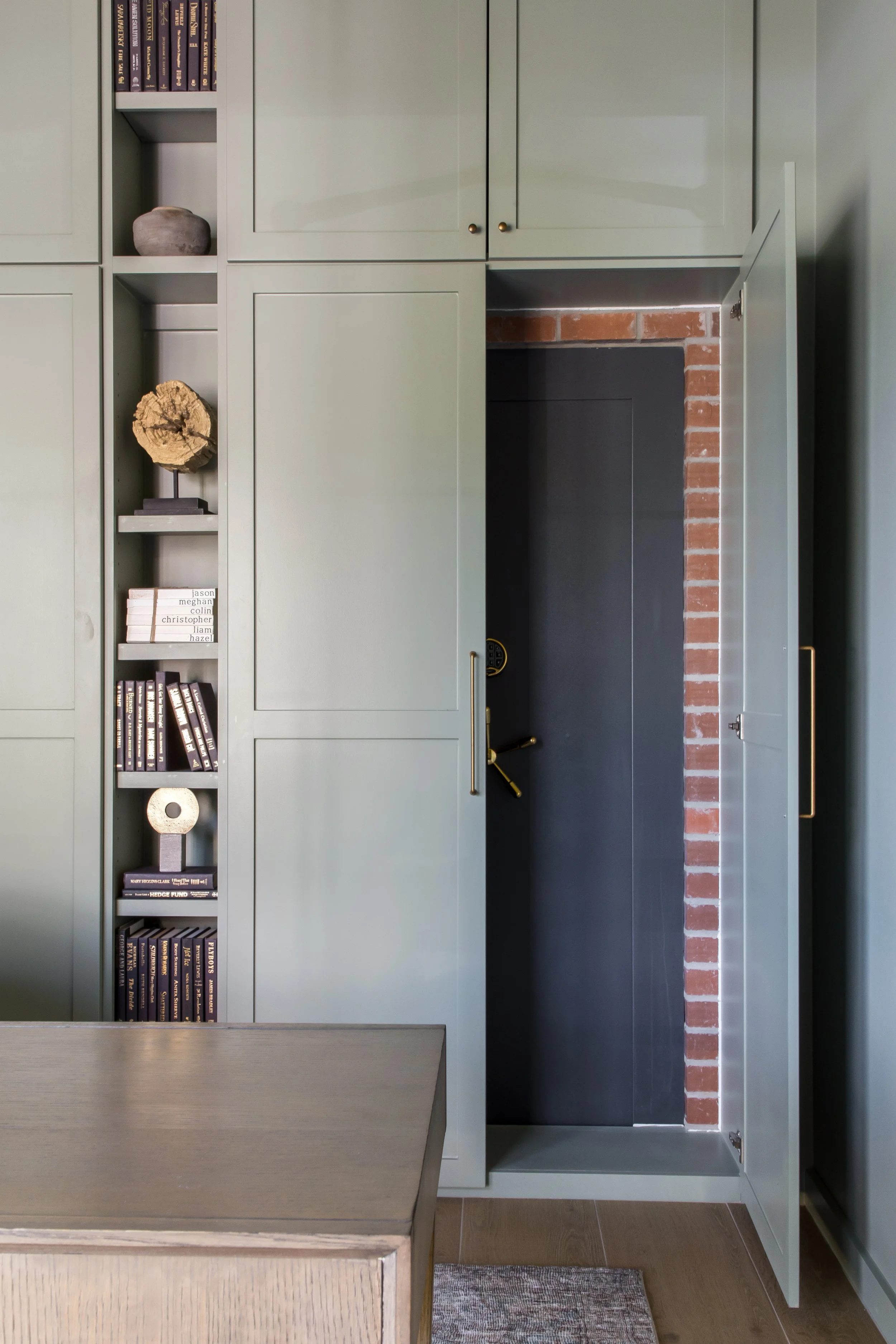 Interior of a room with green built-in cabinets, open cabinet door revealing a safe, and decorative items such as books, a stone, and a wood piece.