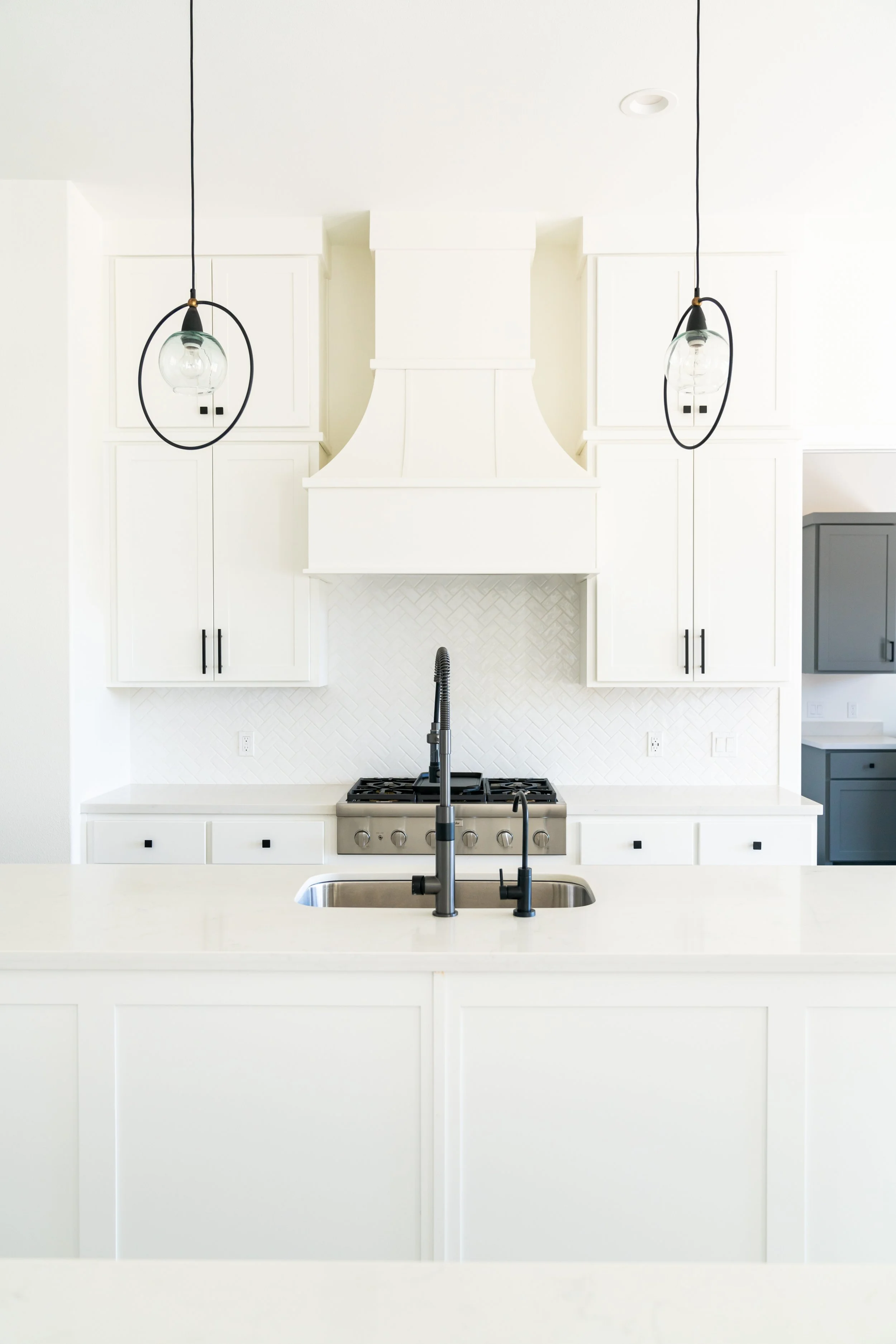White kitchen with black accents, modern pendant lights, gas stove, and a kitchen island with a sink.