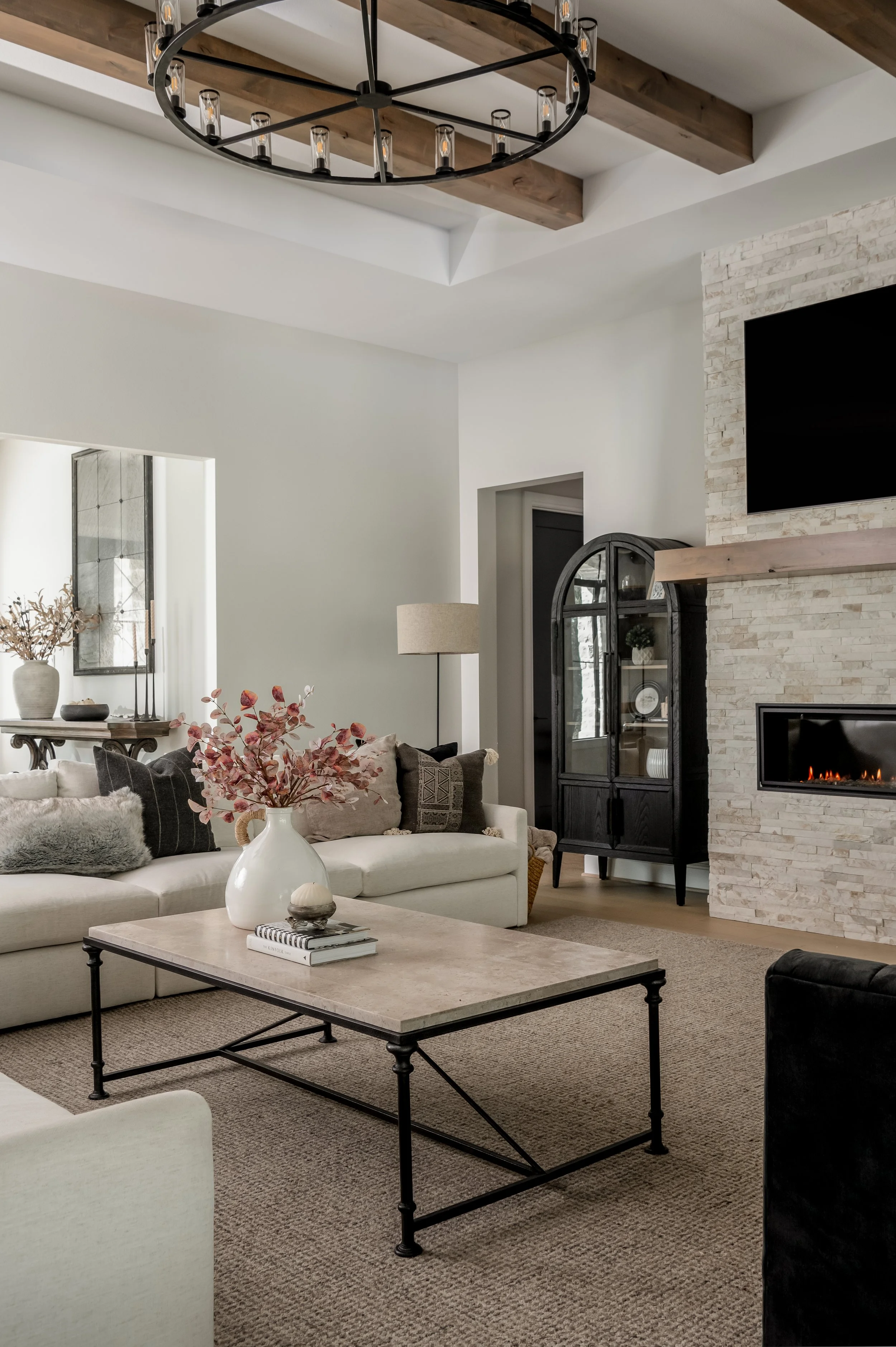 Living room with a white sofa, black and grey pillows, a marble-top coffee table with a white vase and pink flowers, a ceiling light fixture, a brick fireplace, a black display cabinet, and a wall-mounted TV.