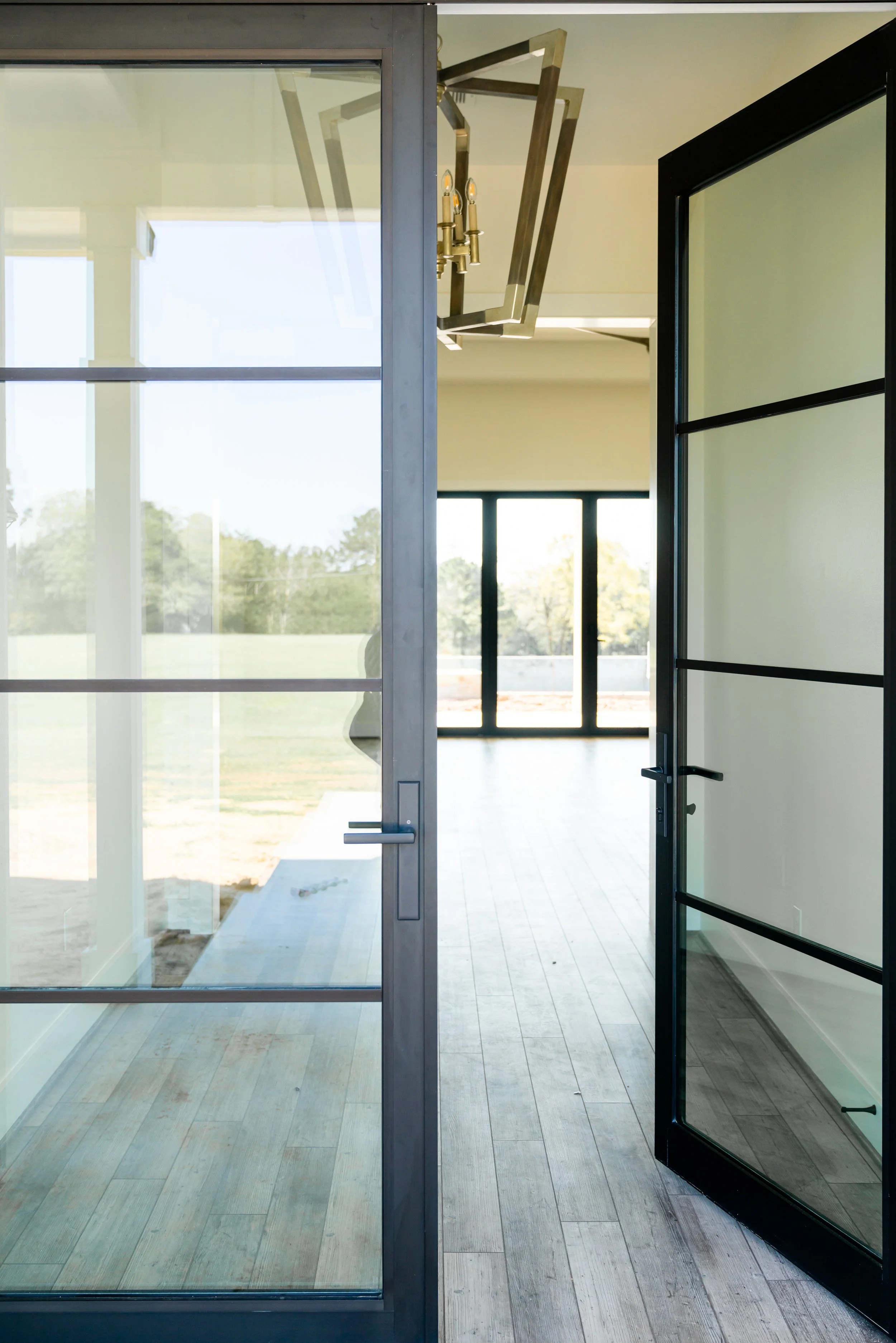 Open glass door leading to a bright, modern interior with large windows and a view of greenery outside.