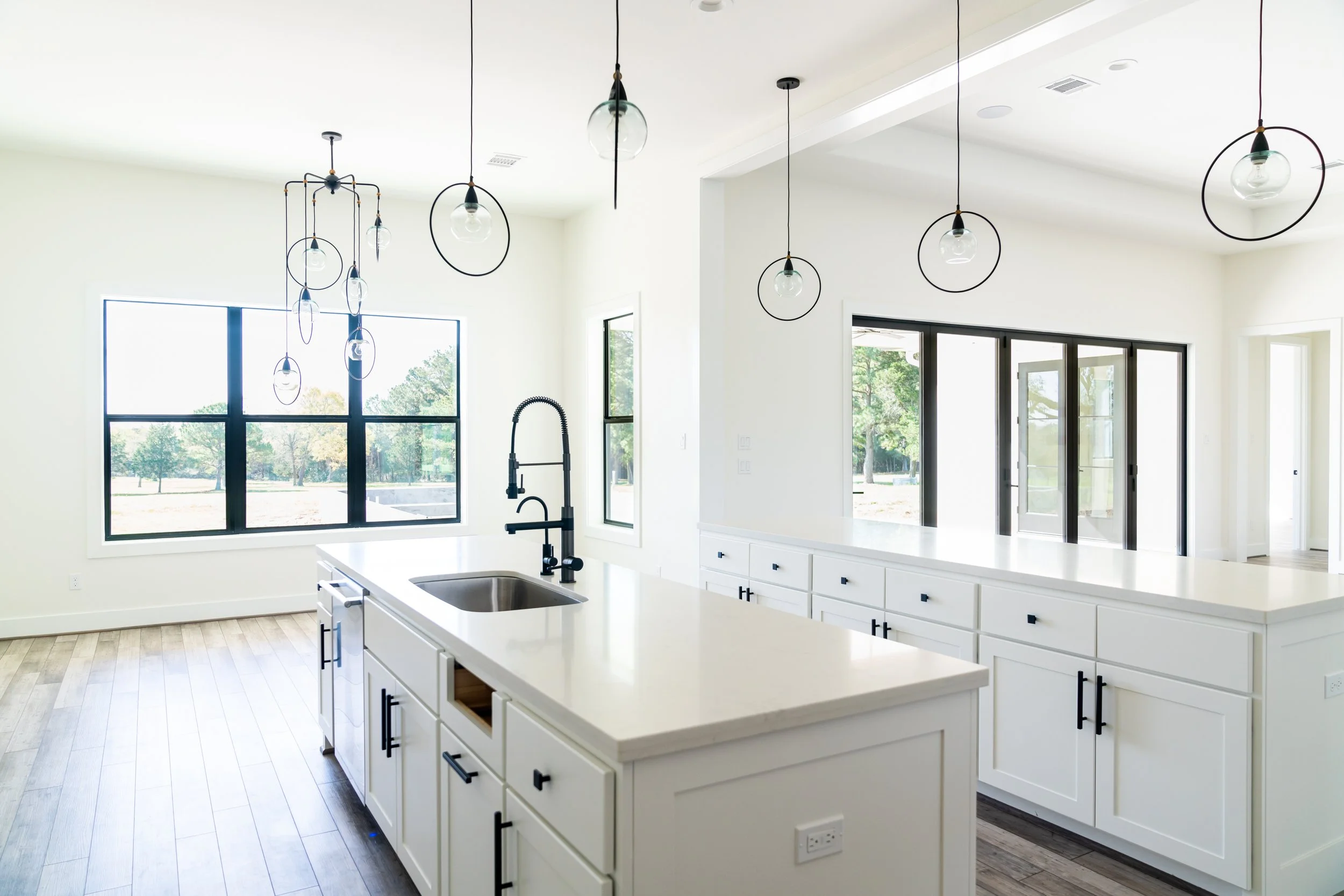 Bright kitchen with white cabinetry, large windows, black hardware, and modern pendant lights.