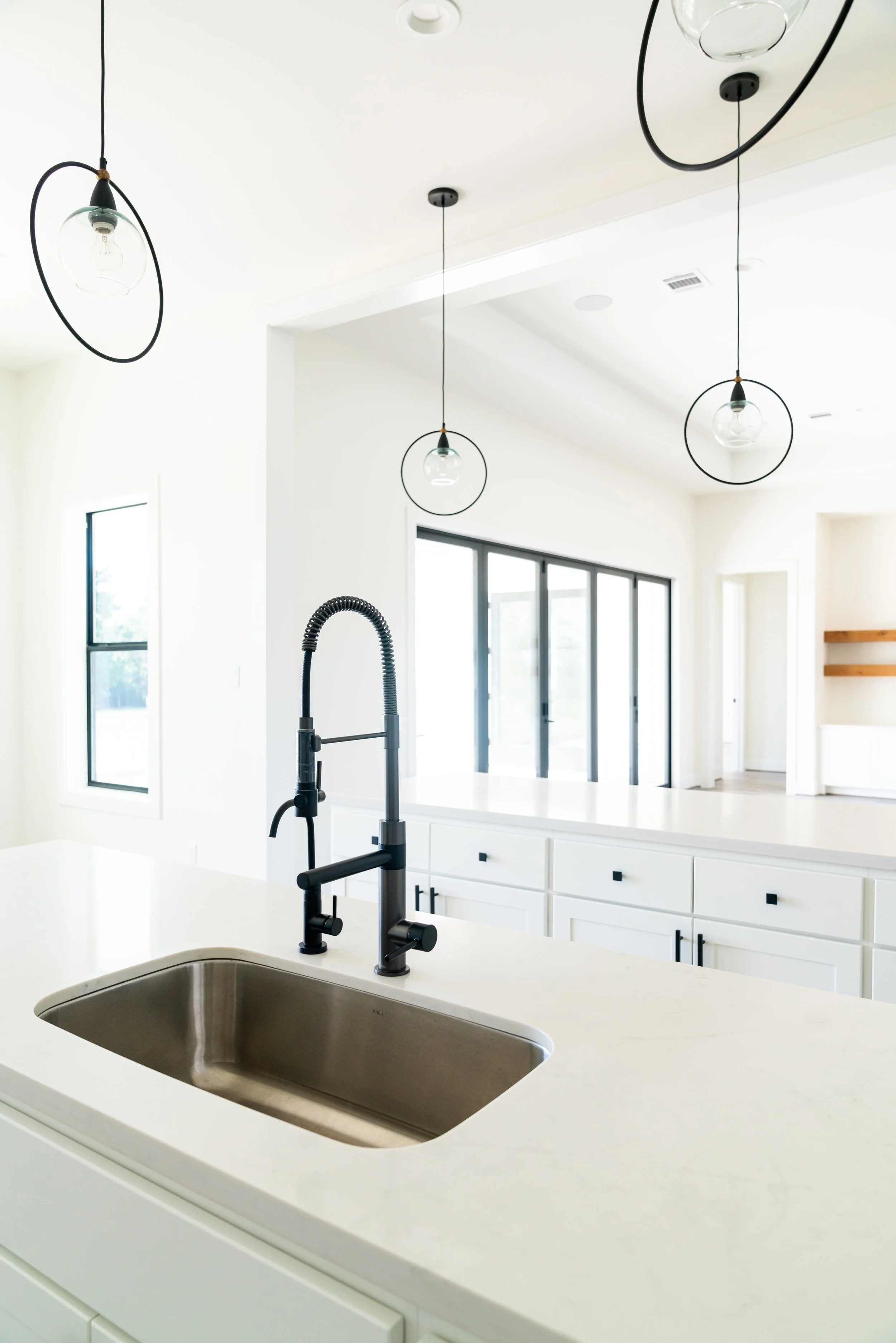 Modern kitchen with white cabinets, a kitchen island, black pendant lights, a black faucet, and large windows.