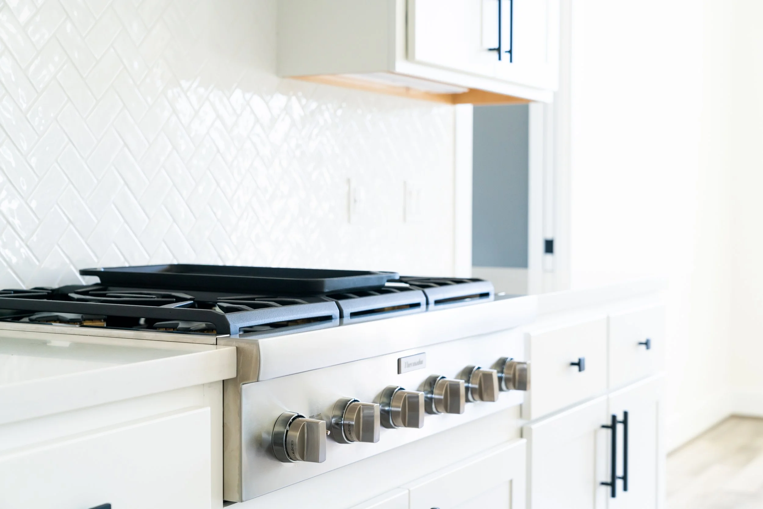 Modern kitchen with a white countertop, a stove with five silver knobs, and a white tile backsplash.