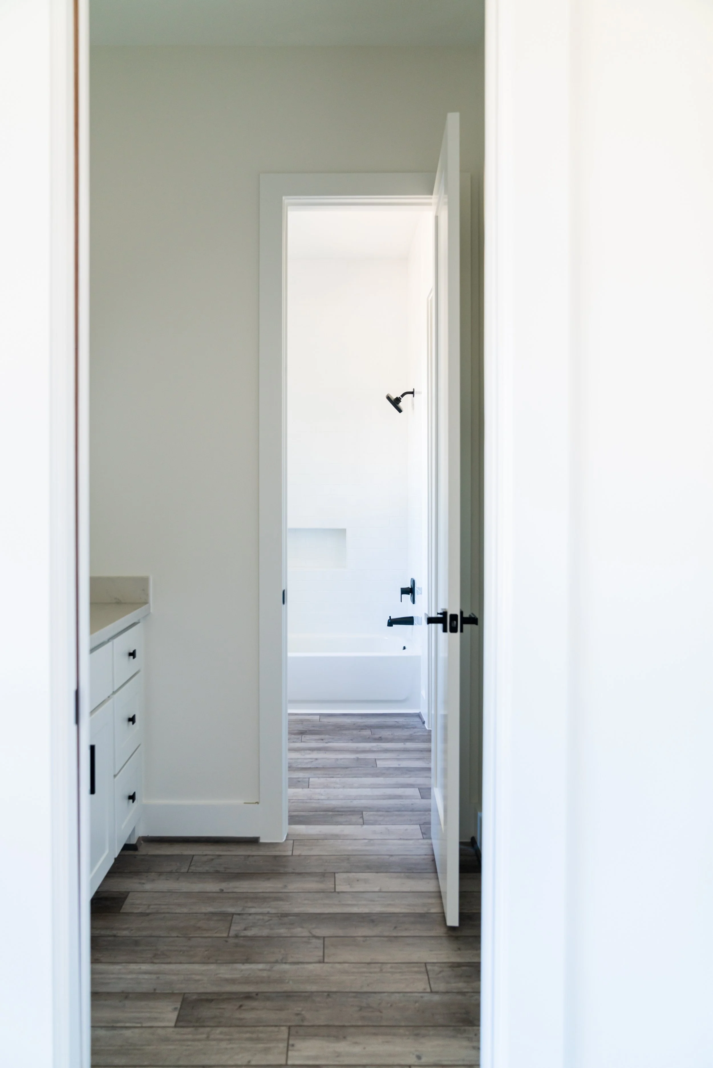Interior view of a bathroom with a doorway leading to a bathtub with a showerhead and dark floorboards.