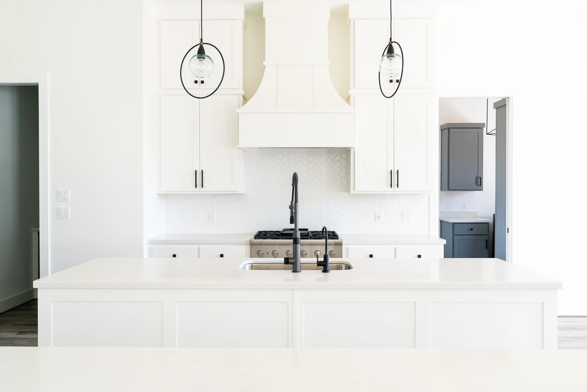 Modern kitchen with white cabinets, a large island with a sink, black faucet, and black pendant lights.