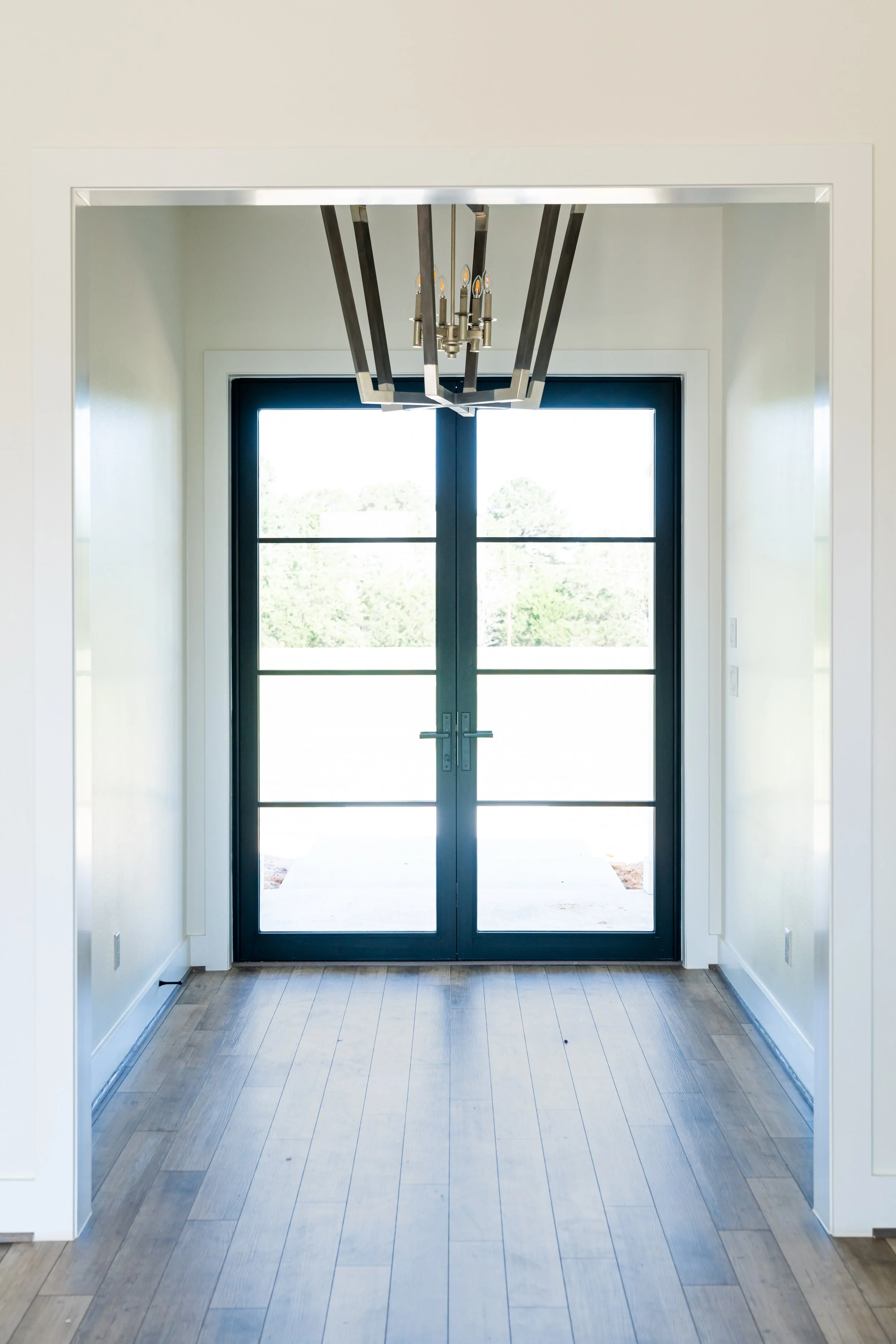 Interior view of a modern entryway with double glass doors and a chandelier hanging from the ceiling.