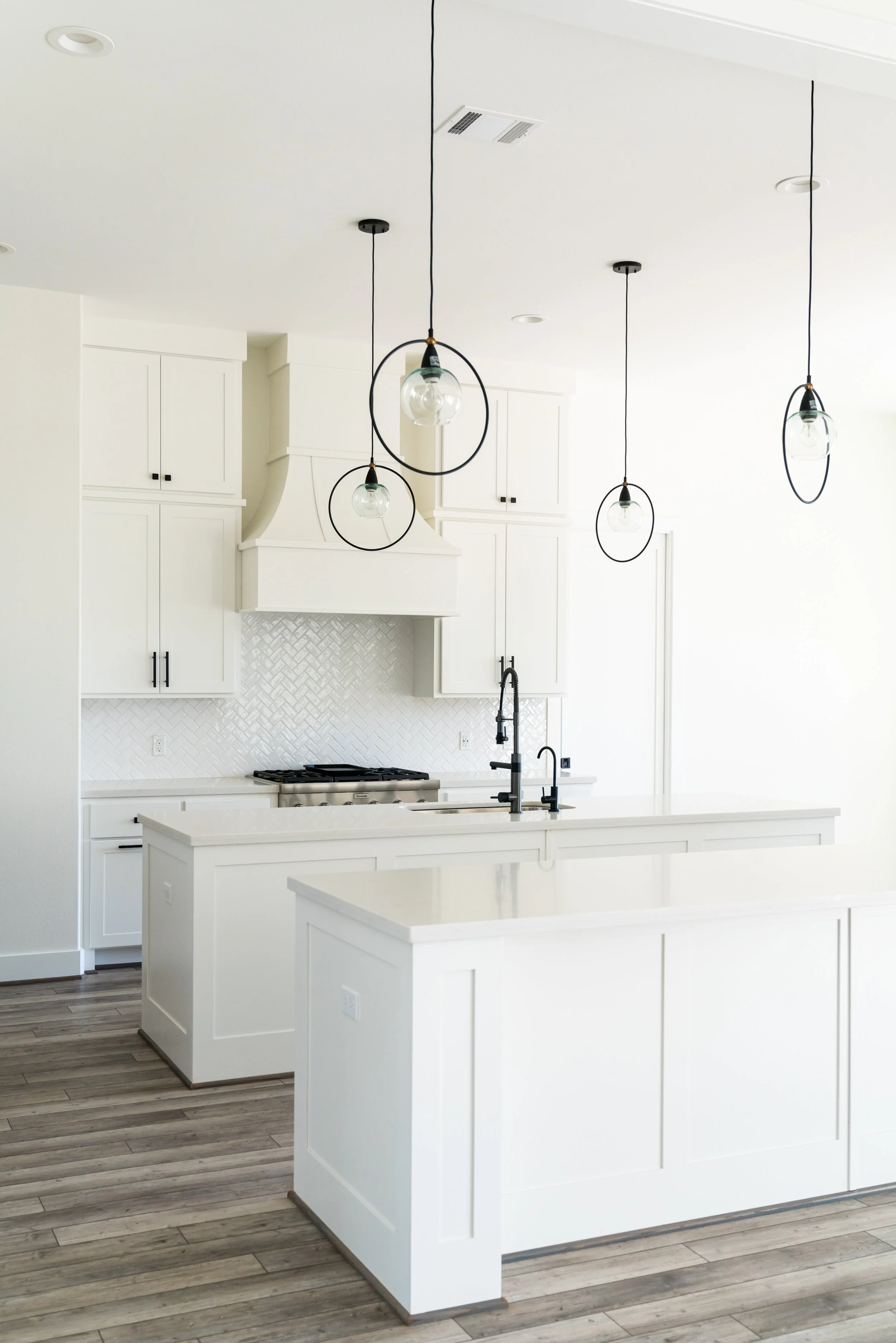 Modern white kitchen with pendant lights and gray wood flooring.