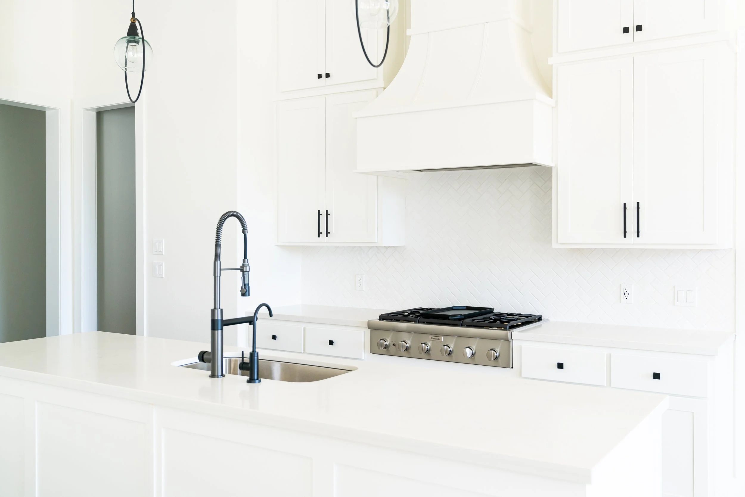Modern white kitchen with a white island, black fixtures, and stainless steel stove, with white cabinetry and subtle backsplash.