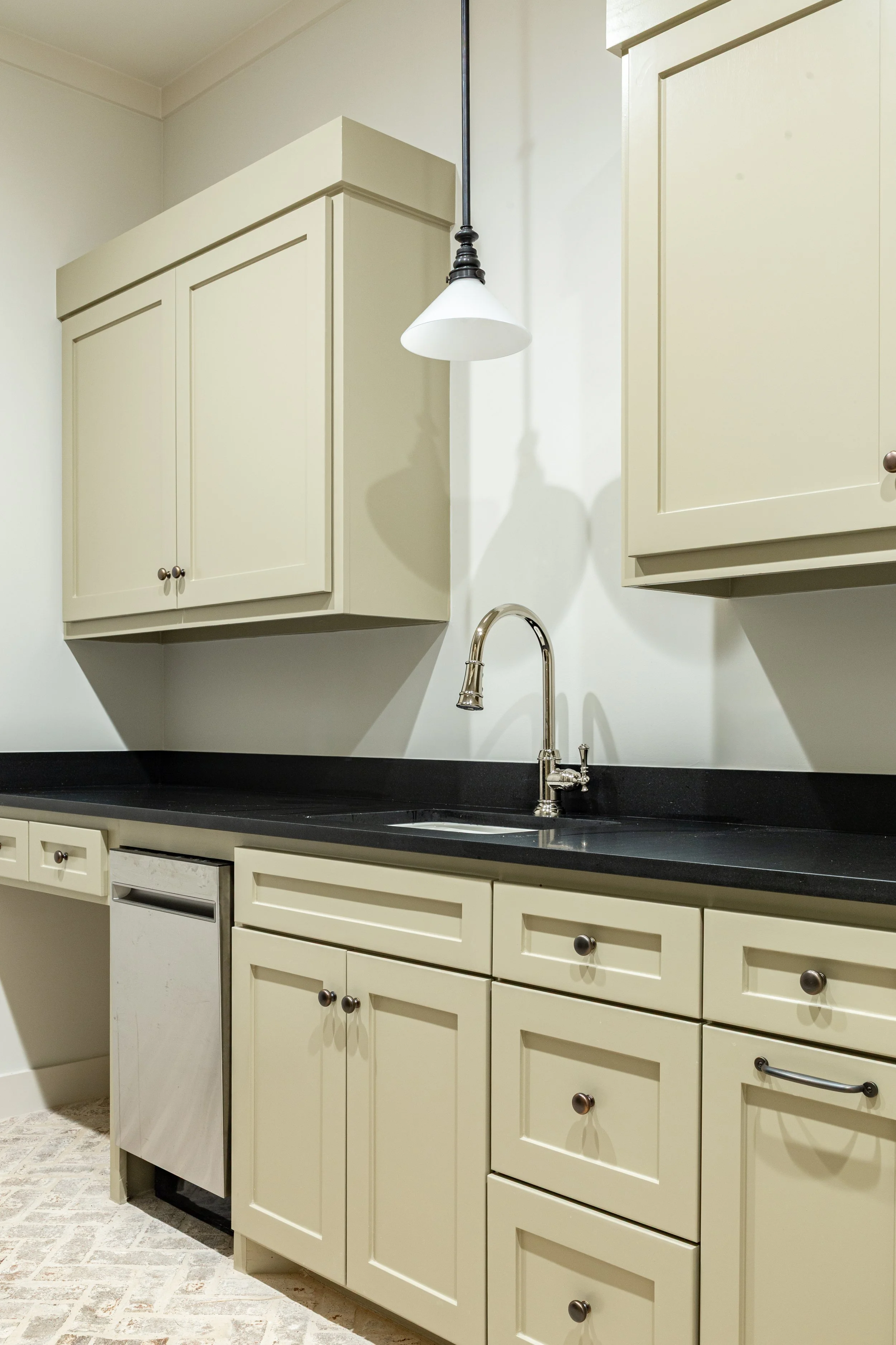 Kitchen with cream-colored cabinets, black countertop, a stainless steel faucet over a sink, and a white pendant light hanging from the ceiling.