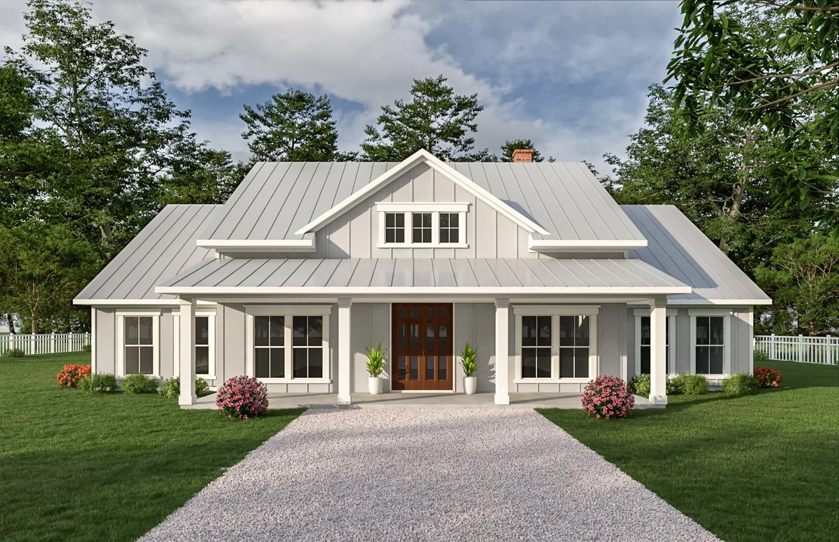 Front view of a white house with a metal roof, surrounded by green lawn and trees, featuring a gravel driveway and potted plants near the entrance.