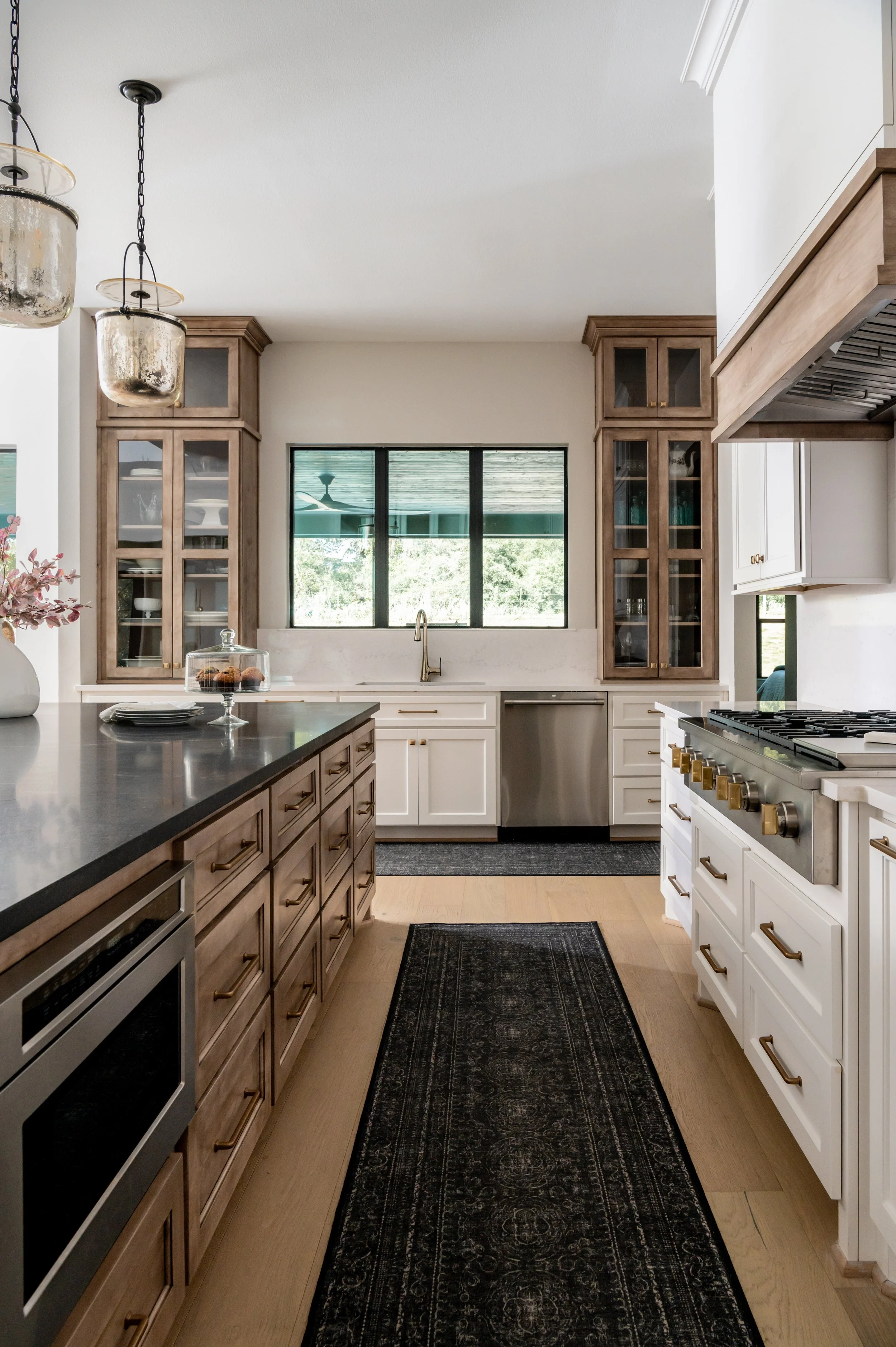 Modern kitchen with black countertop island, white and wood cabinetry, stainless steel appliances, and a window above the sink.