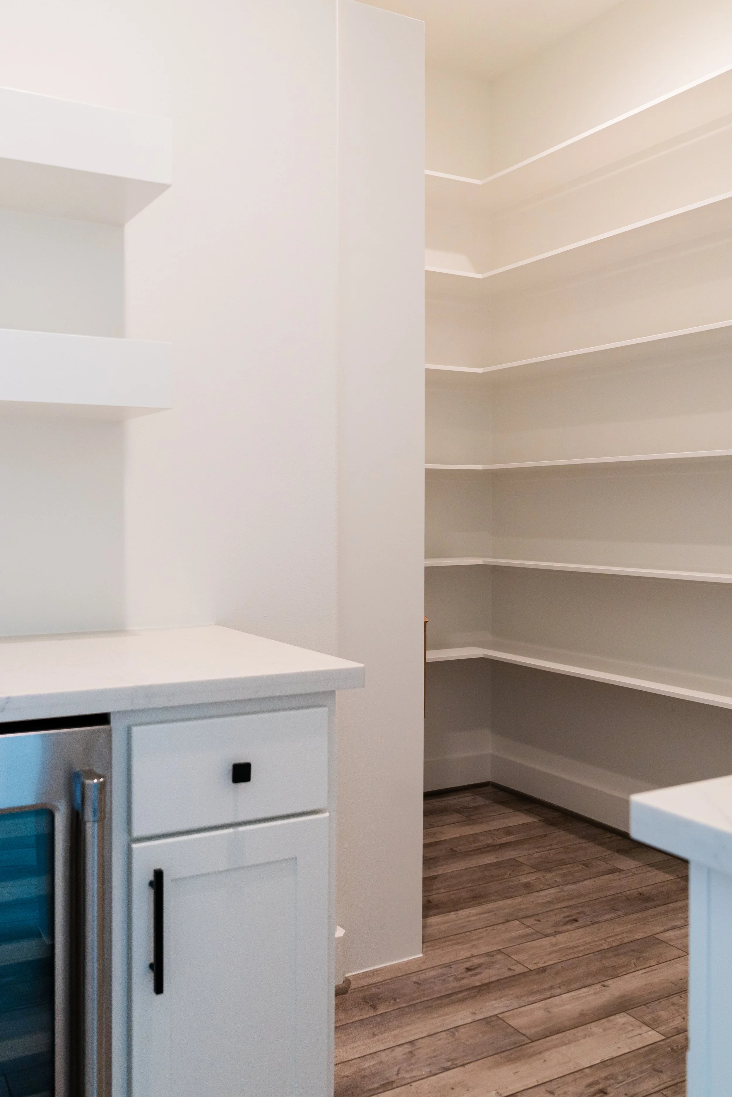 Empty pantry with white shelves and wood-look flooring.