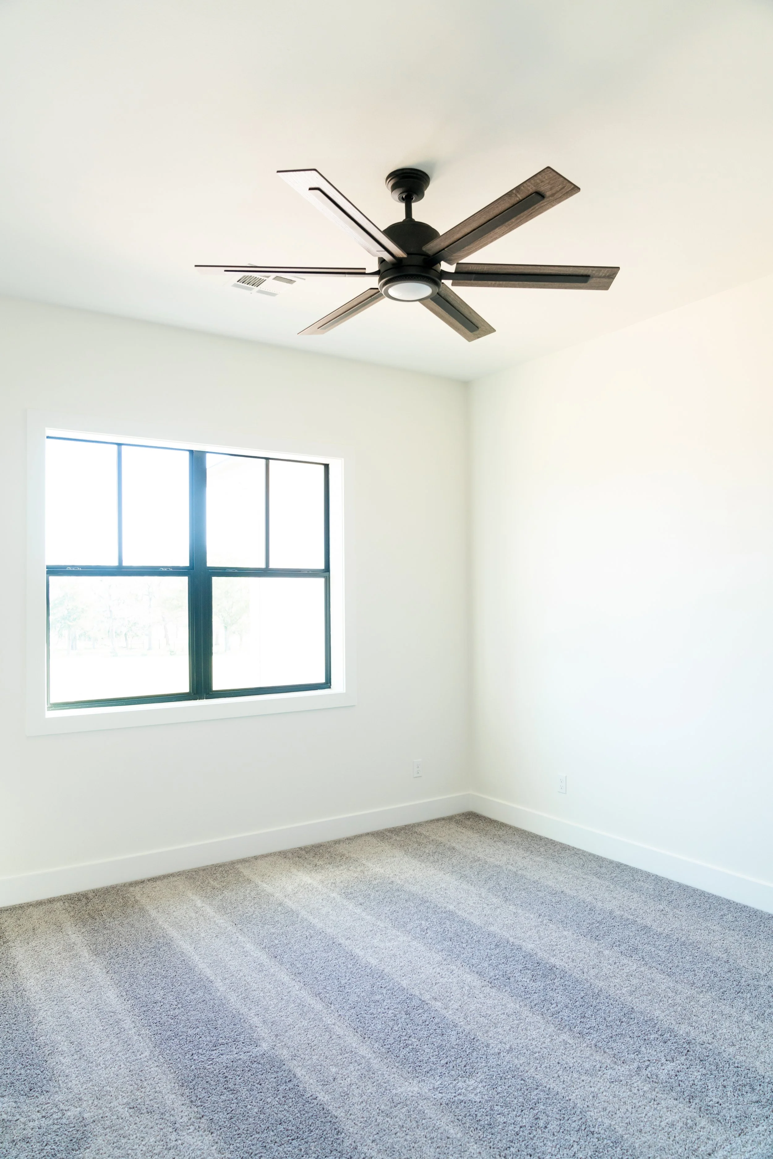 Empty room with white walls, gray carpet, window, and modern ceiling fan.