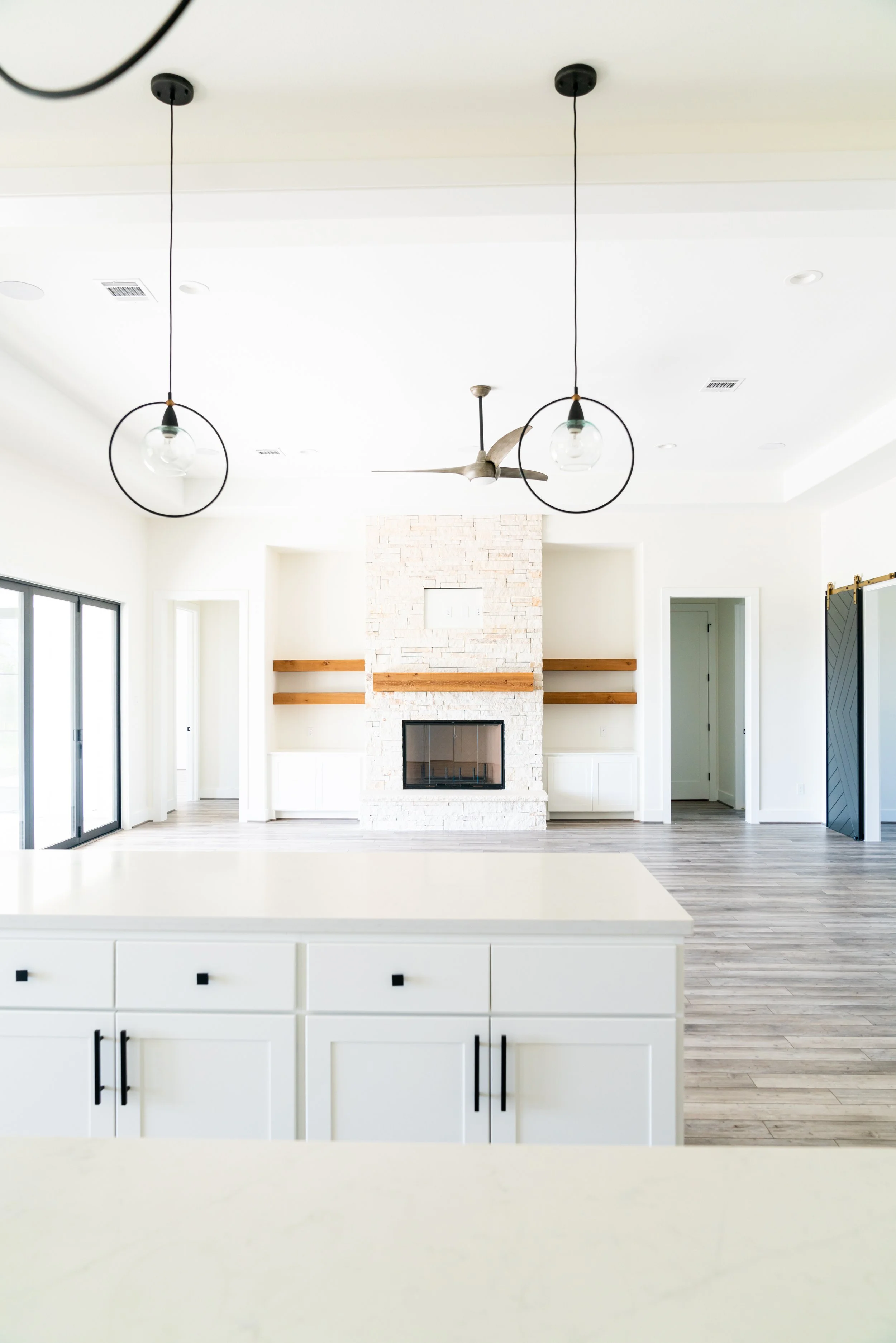 Modern living room with white fireplace, wooden shelves, stainless steel ceiling fan, and pendant lights.