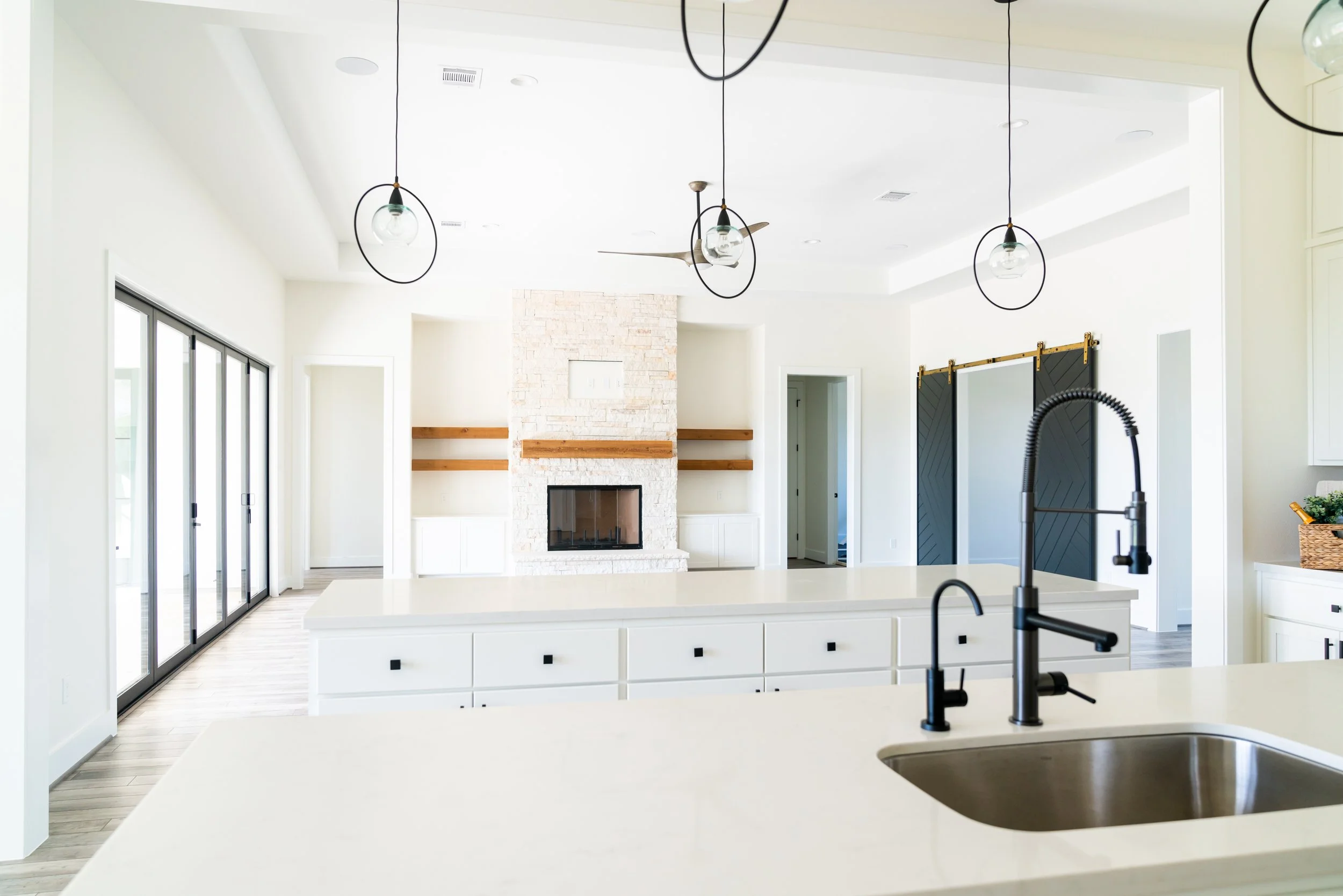 Modern kitchen with white cabinets and countertops, black fixtures, a fireplace with a brick surround, sliding glass doors, pendant lights, and a sliding barn door.