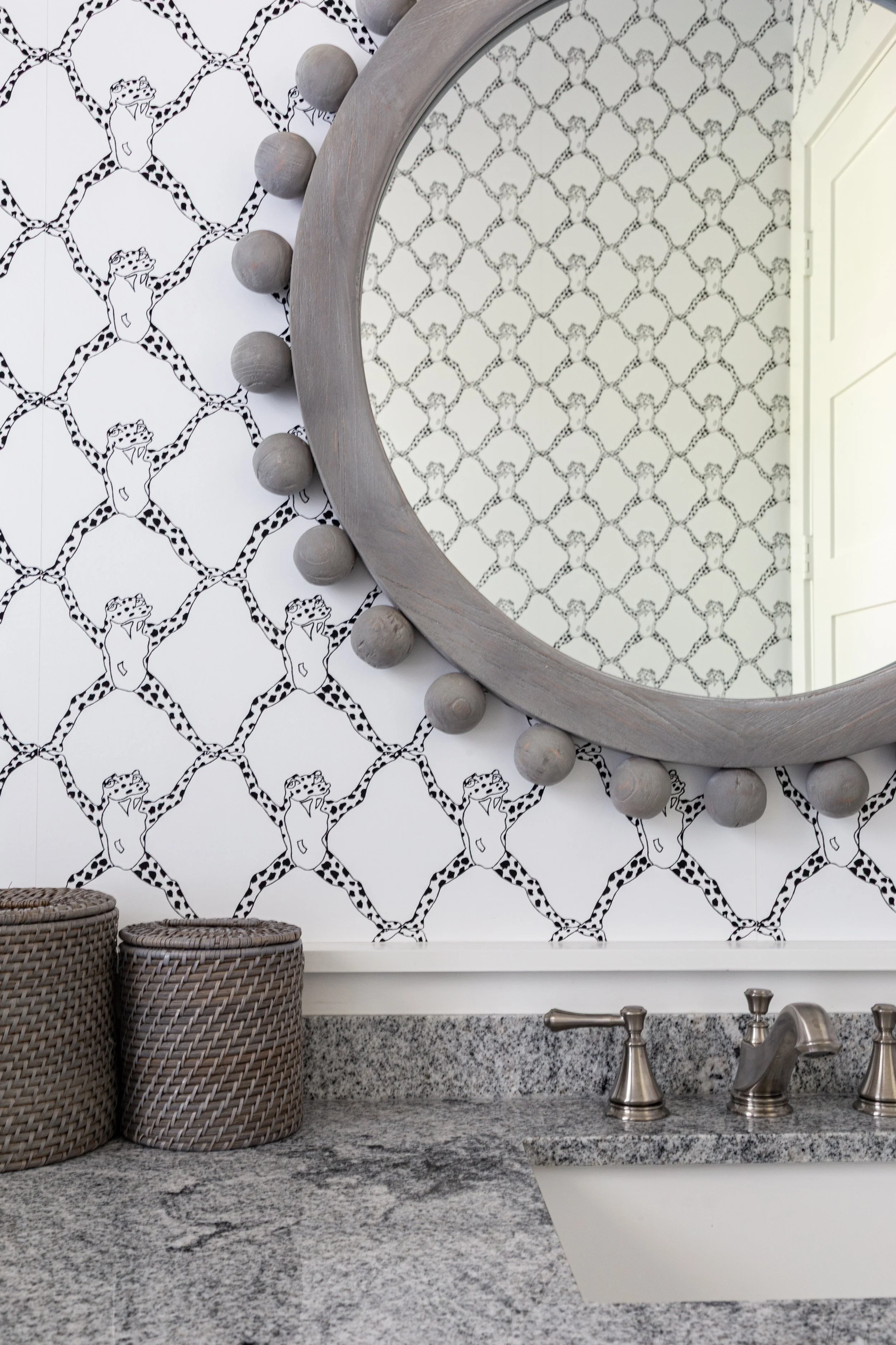 Decorative bathroom with black and white animal print wallpaper, round mirror with bulb accents, granite countertop, and woven baskets.