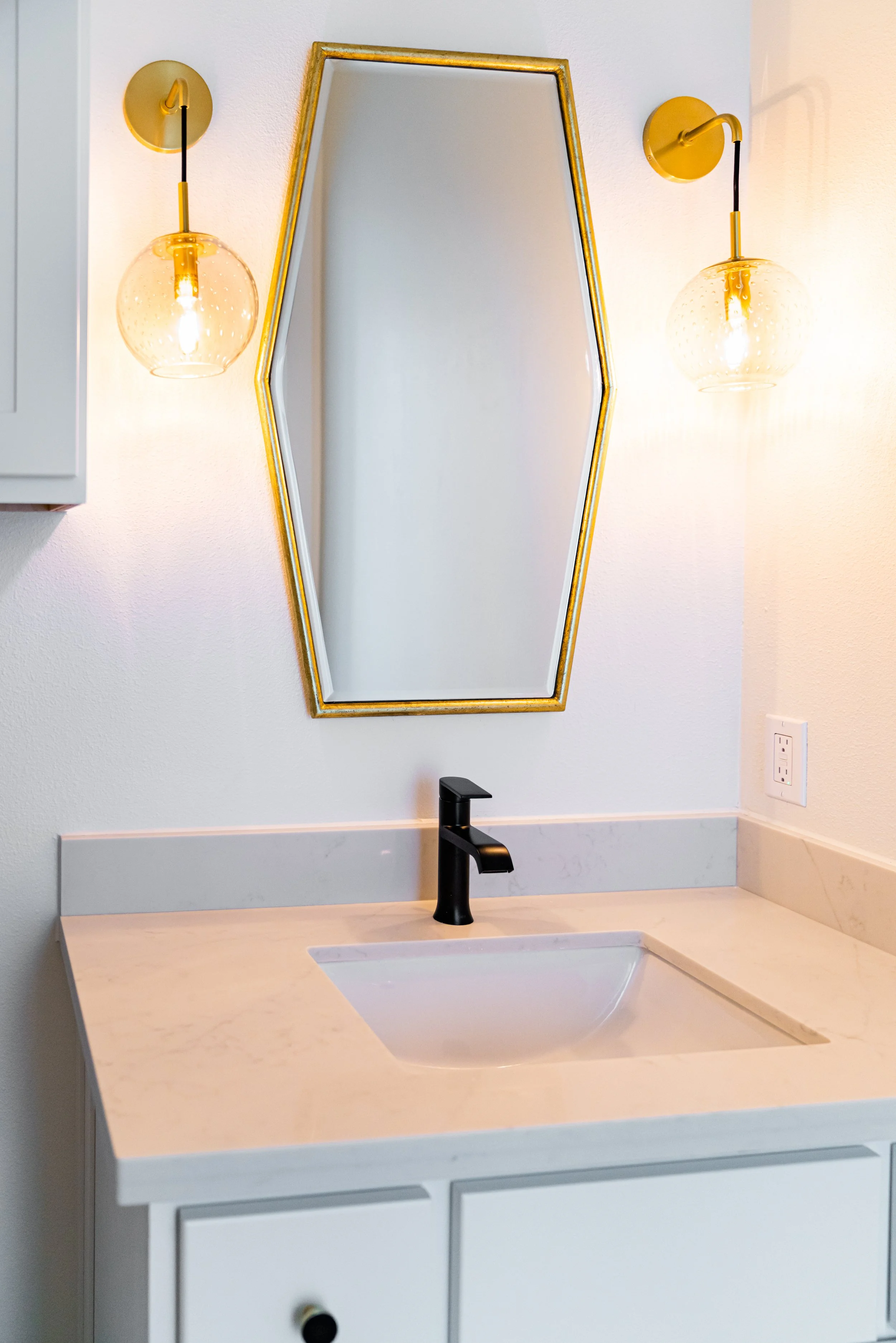 Bathroom sink with black faucet, white marble countertop, and a mirror above it, flanked by two yellow wall-mounted light fixtures.