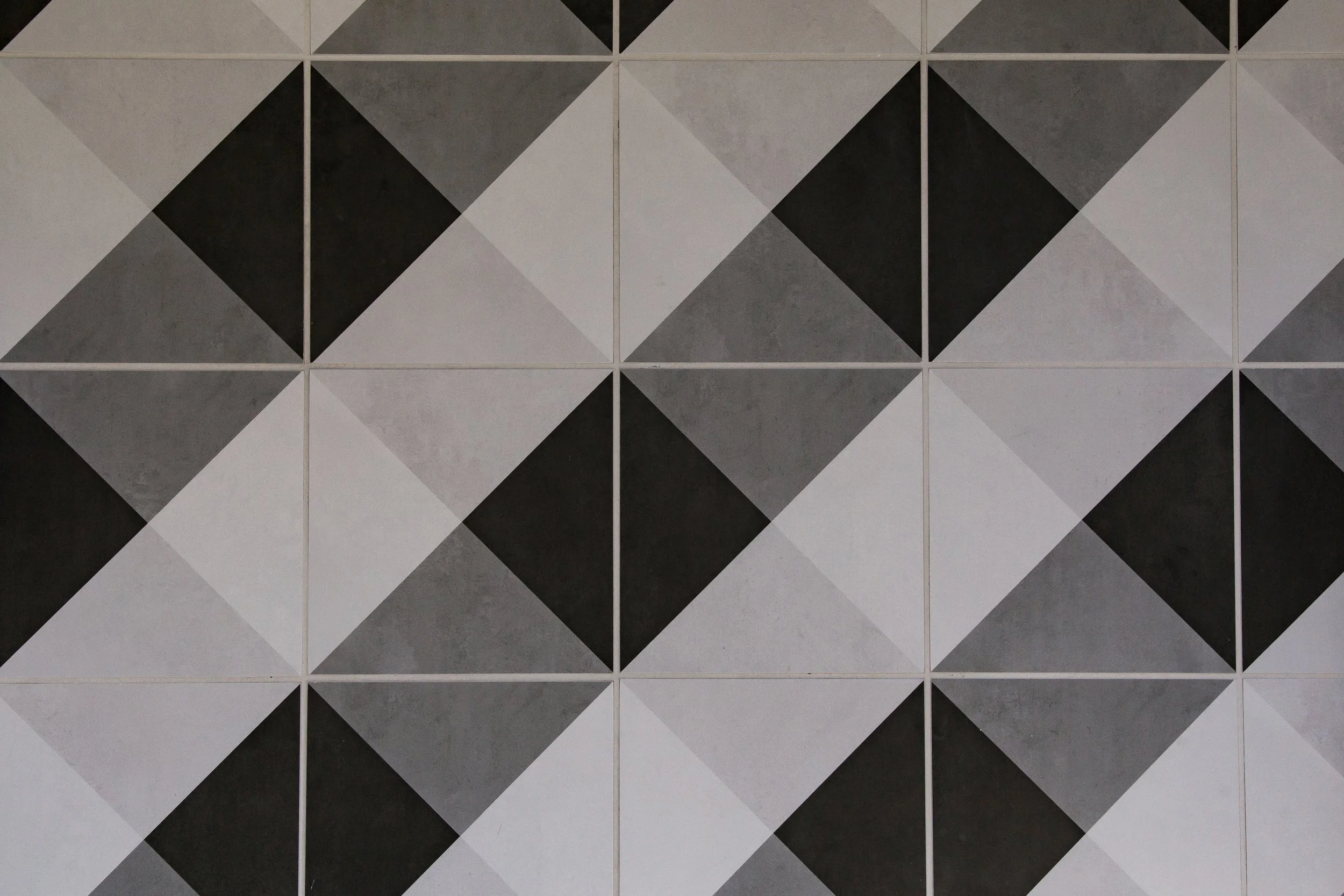 Wall with a geometric pattern consisting of tiles arranged in a diamond and square pattern in shades of black, white, and gray.