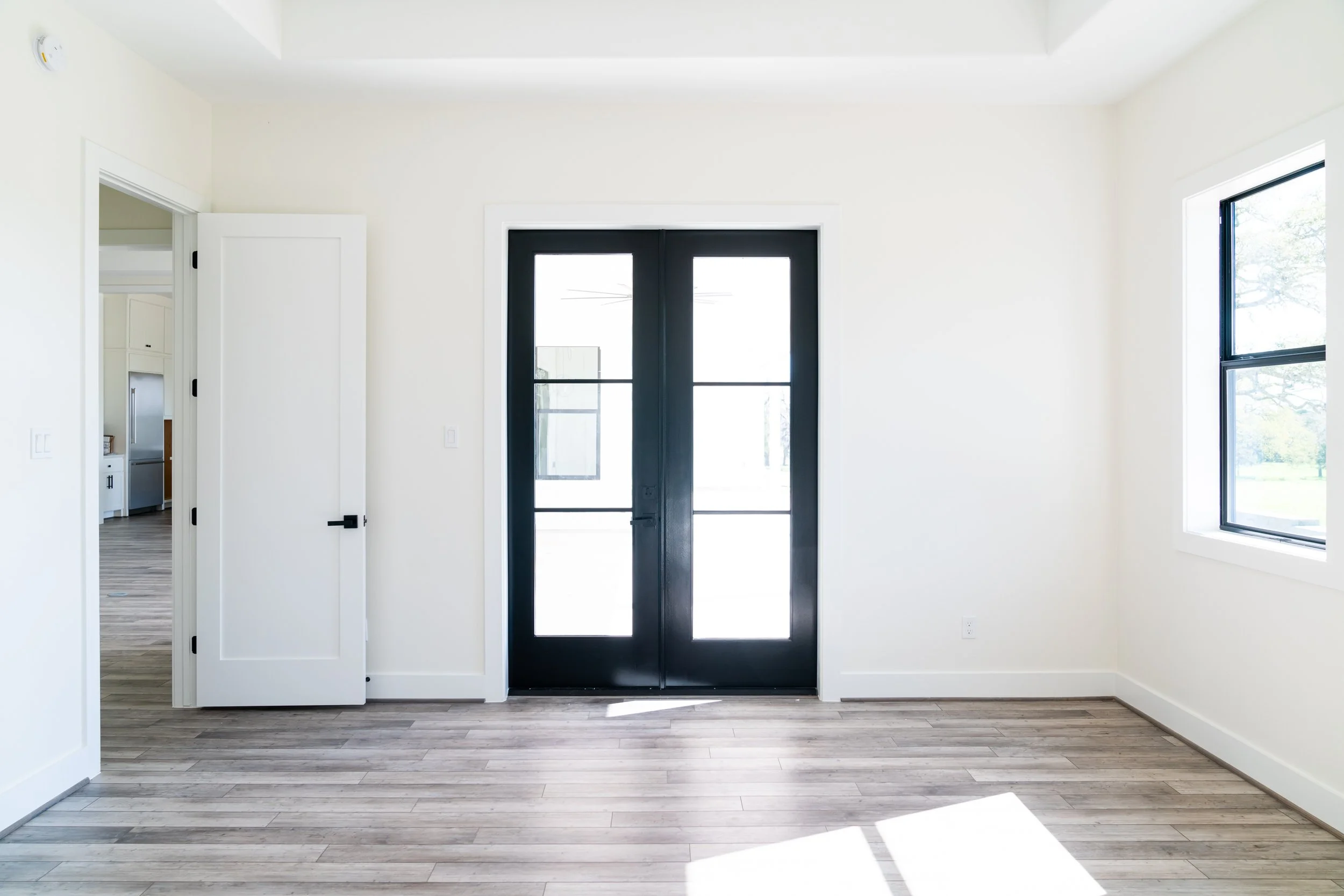 Empty room with white walls, large windows, and a black front door with glass panels.