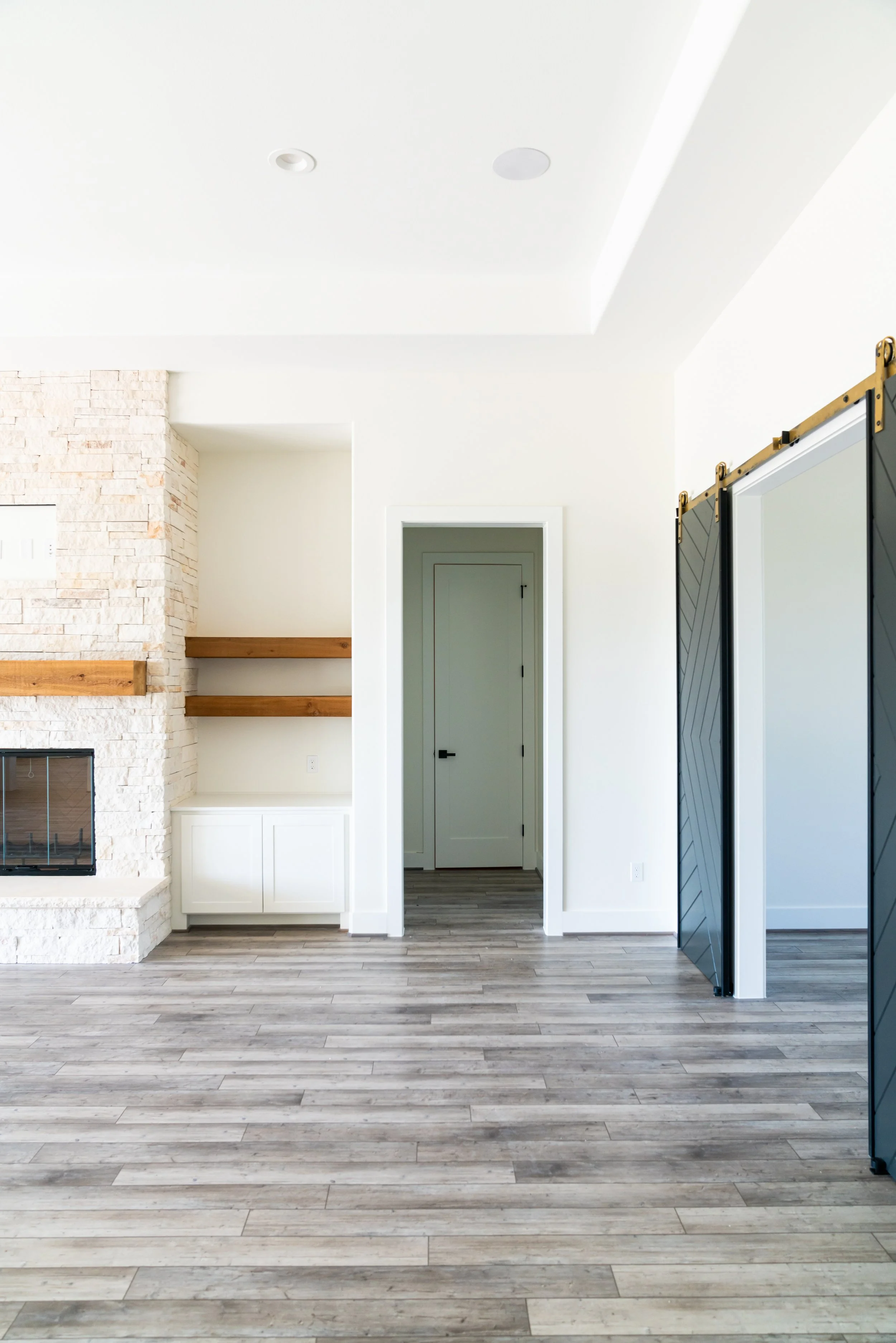 Empty living room with white walls, wood floor, gas fireplace, and decorative sliding barn doors.