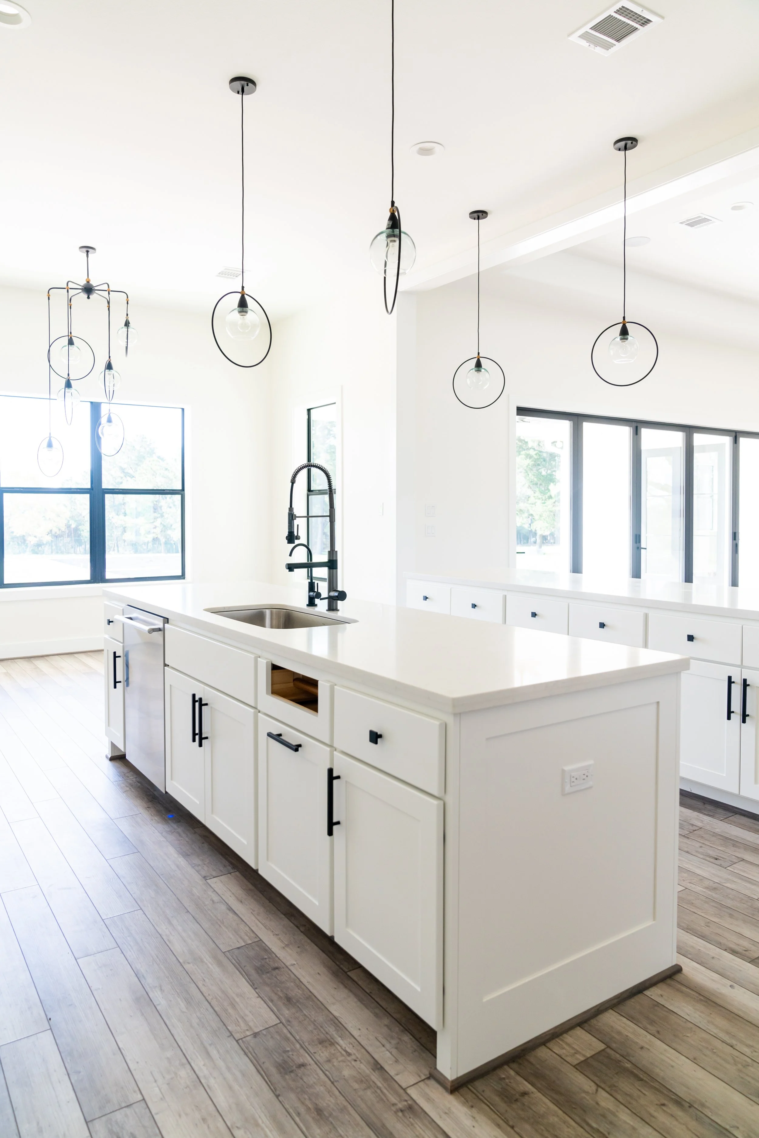 Modern kitchen with white cabinets, wood flooring, pendant lights, and large windows.