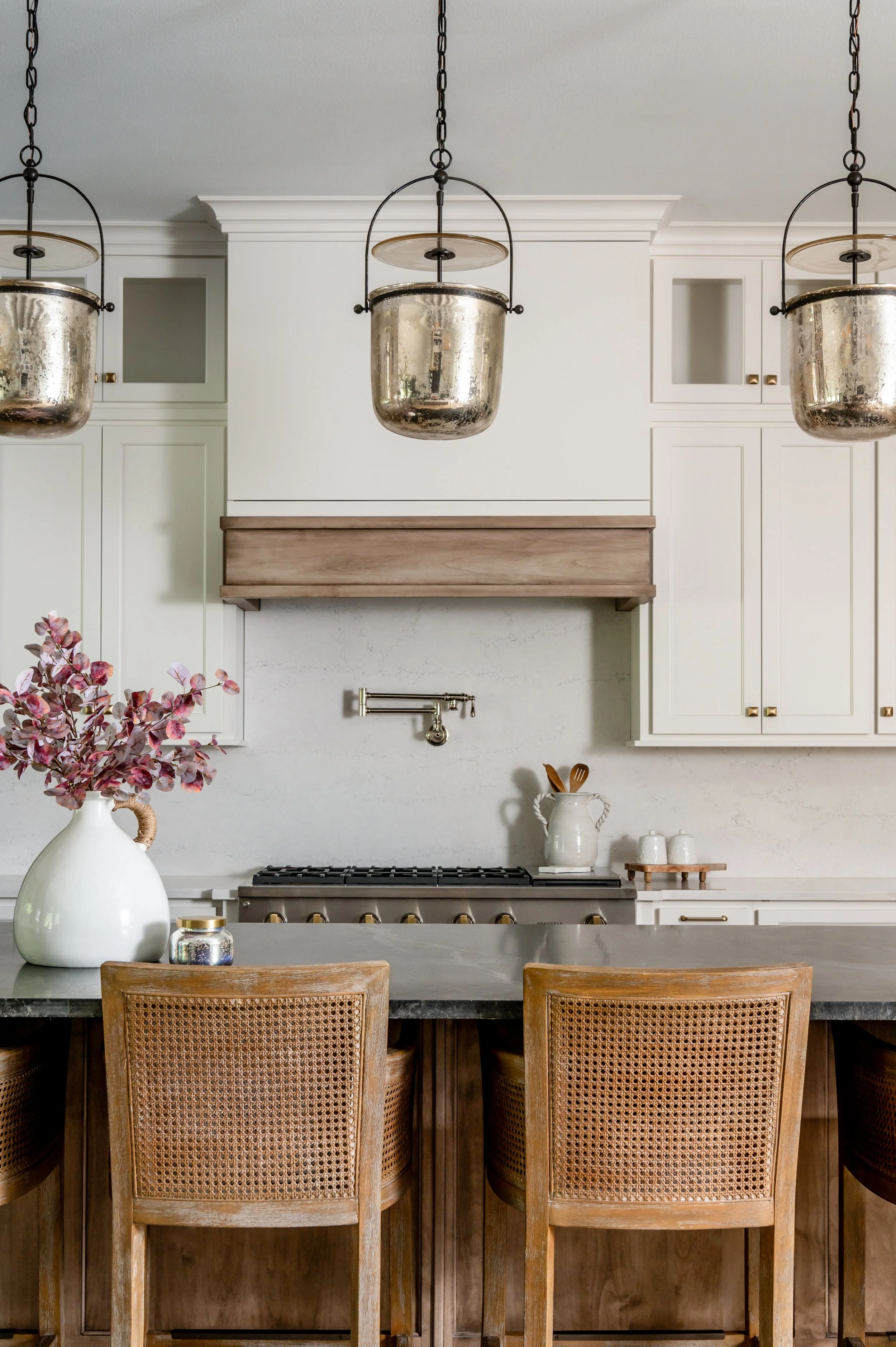 Modern kitchen with white cabinets, a granite countertop, a stove, and pendant lighting fixtures above a kitchen island with wooden chairs.