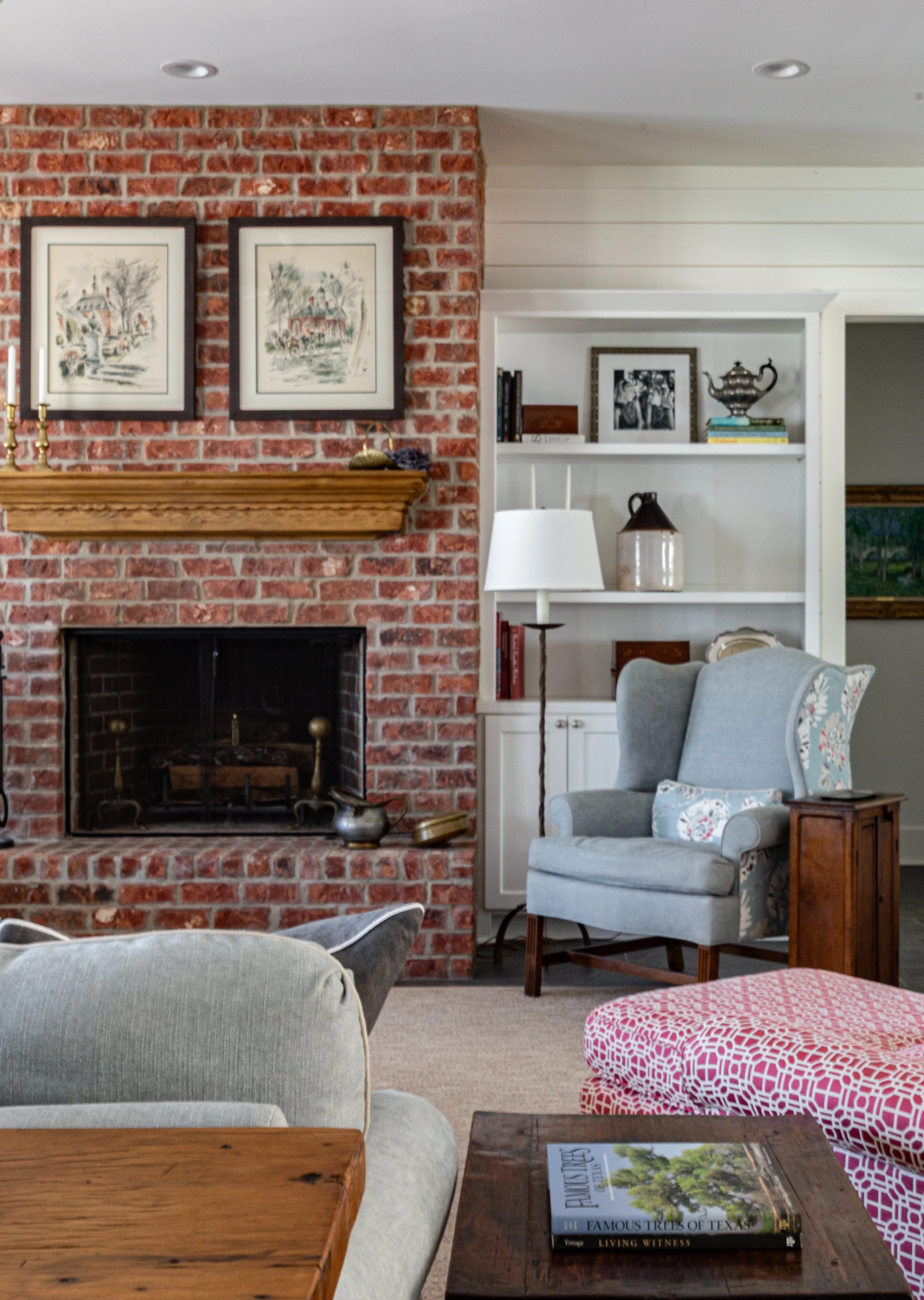 Living room with brick fireplace, armchair, bookshelf, and decorative items.